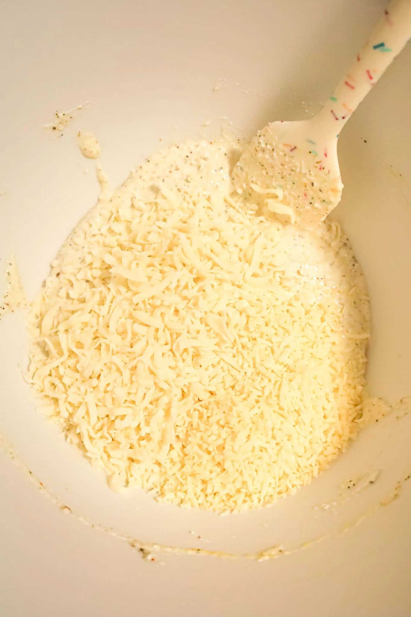 shredded cheese on top of sour cream and ricotta mixture in a mixing bowl