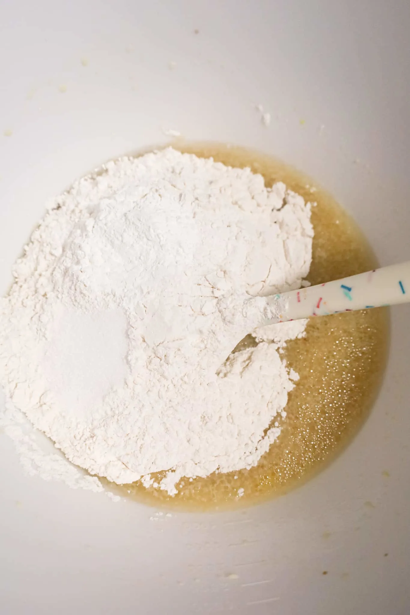 baking powder and flour on top of oil and milk mixture in a mixing bowl