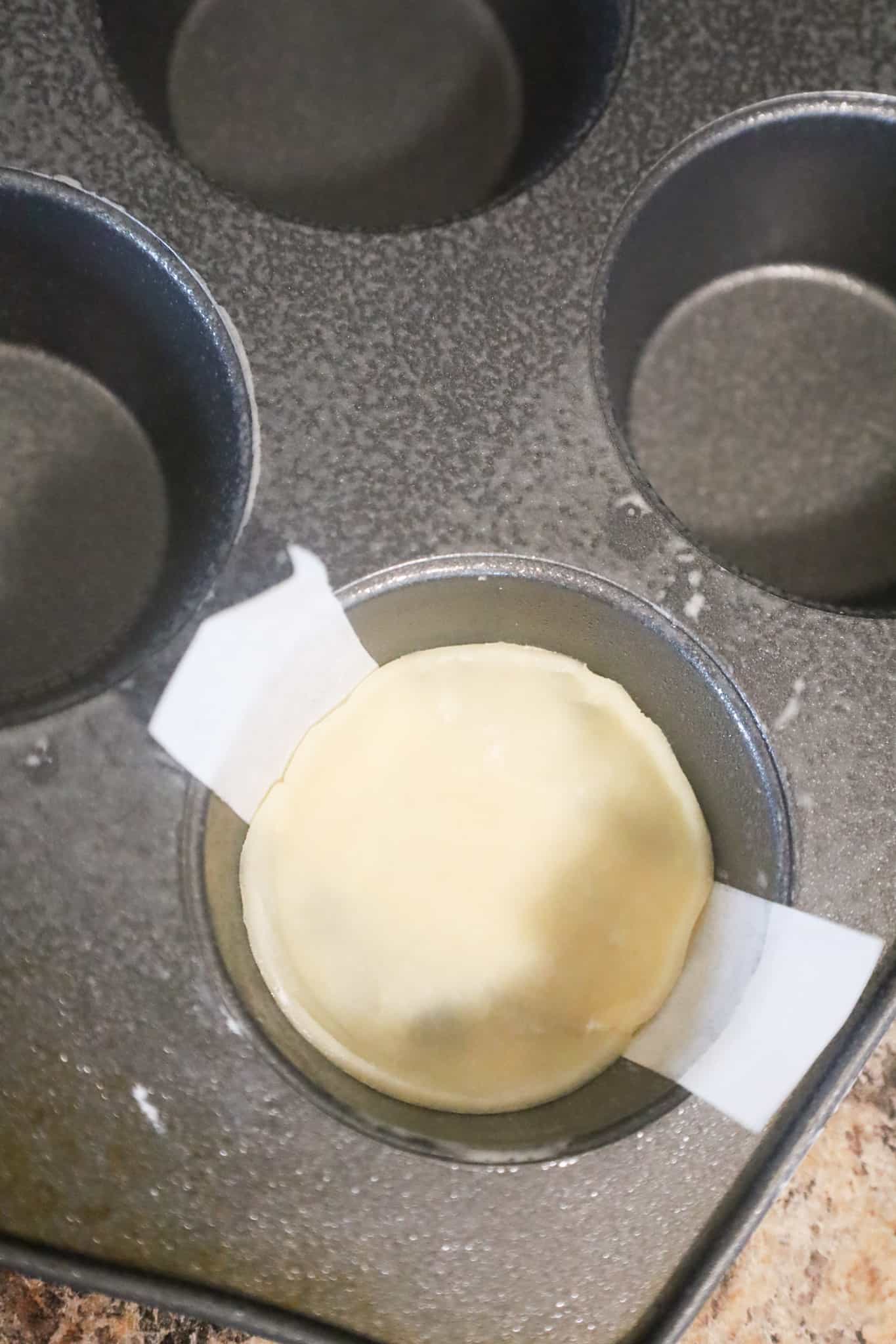 pastry on top of parchment strip in a muffin tin