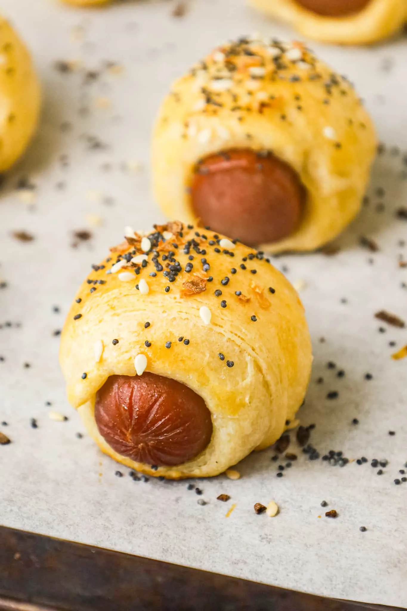 Pigs in a Blanket are a delicious bite sized party food or kid friendly dinner recipe using wieners and Pillsbury crescent roll dough topped with poppy seeds, sesame seeds and dehydrated minced onions.