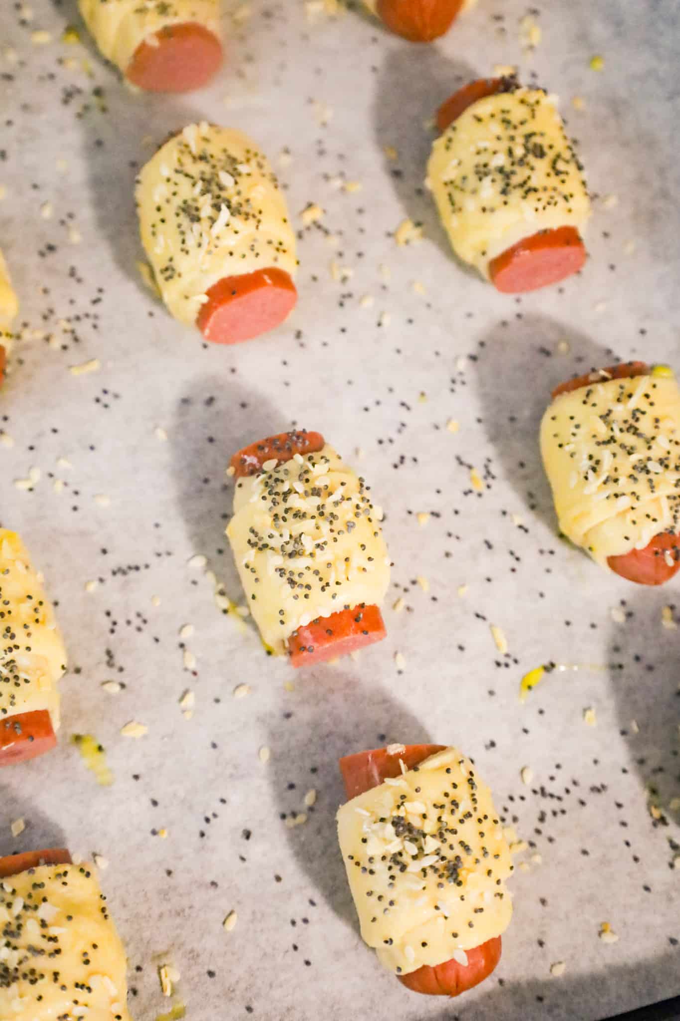 poppy seeds and sesame seeds on top of crescent wrapped hot dog pieces on a parchment lined baking sheet
