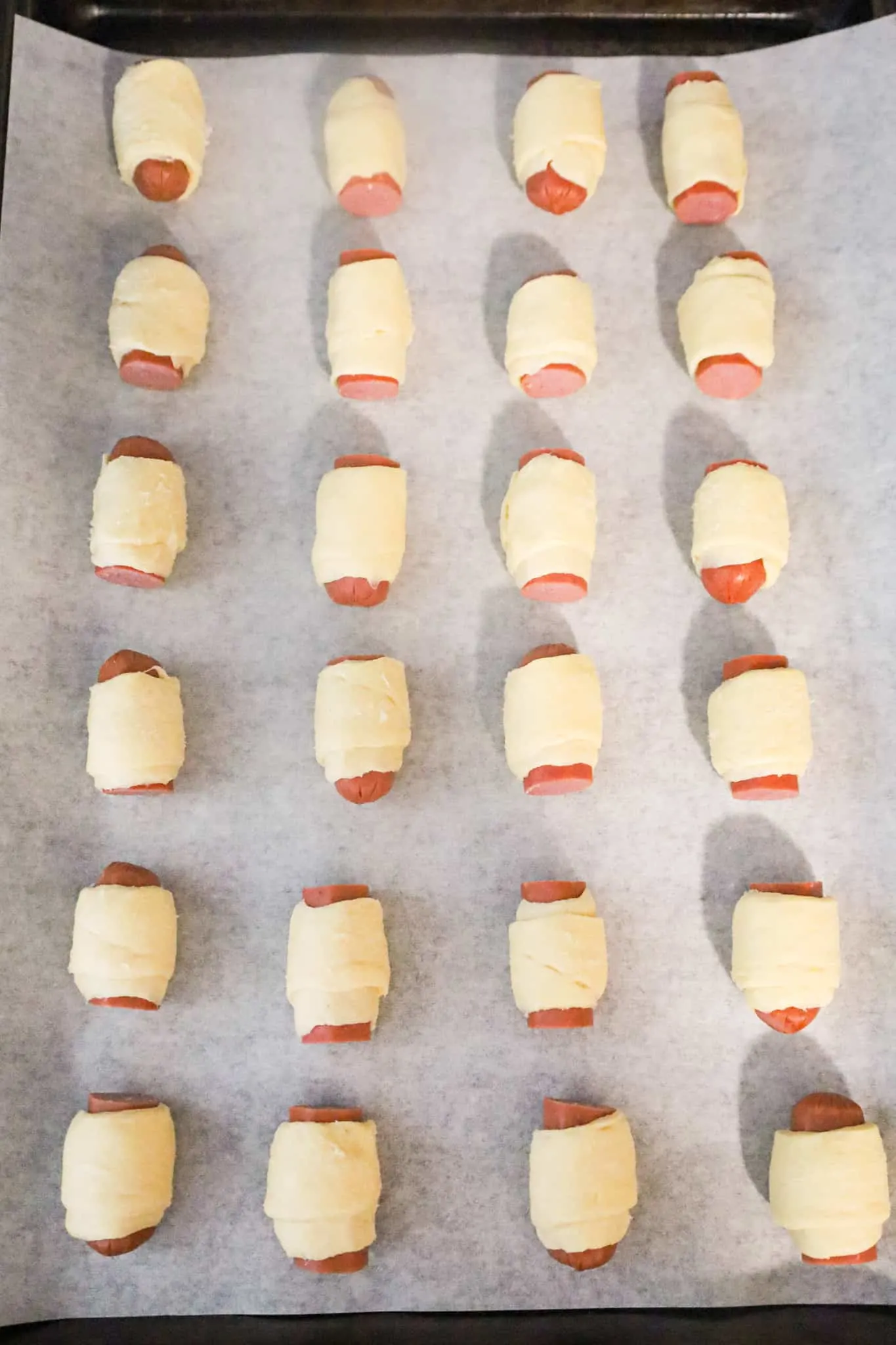 hot dog pieces wrapped in crescent dough on a parchment lined baking sheet