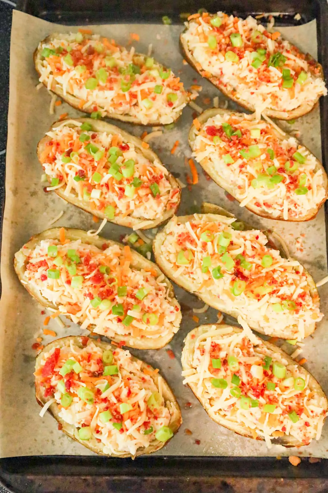 chopped green onions, crumbled bacon and cheese on top of mashed potato in potato skins