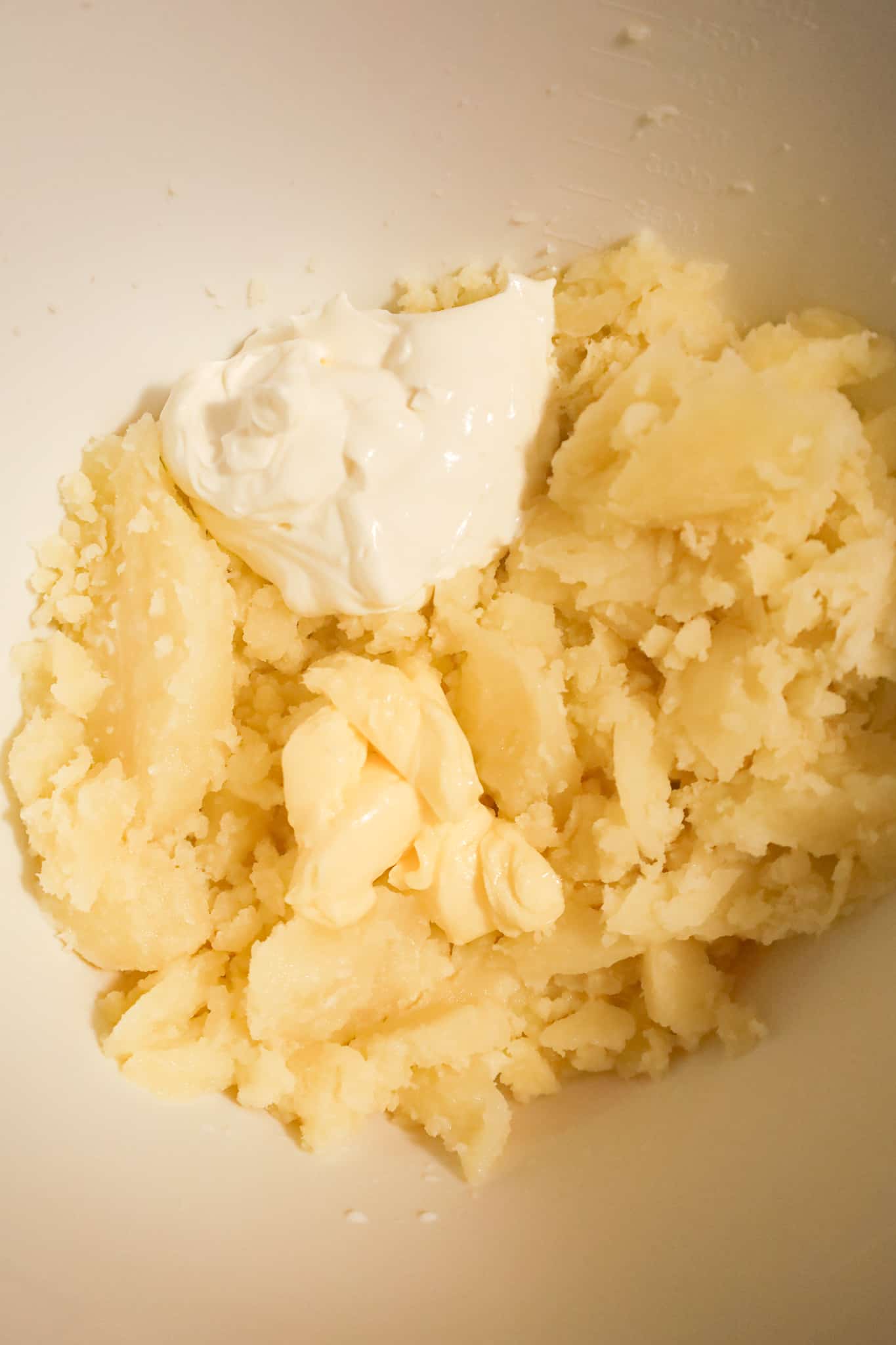 butter and sour cream on top of cooked potato in a mixing bowl