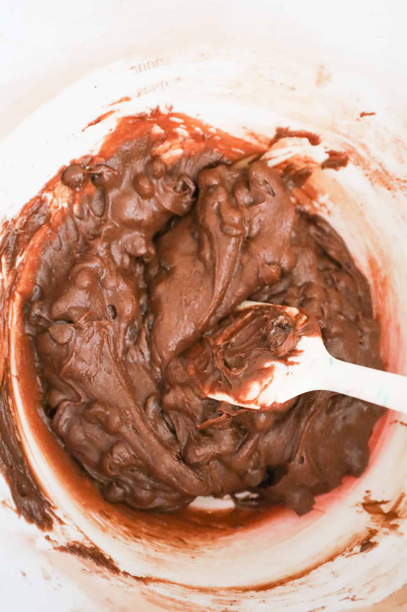 chocolate chips being stirred into brownie batter in a mixing bowl