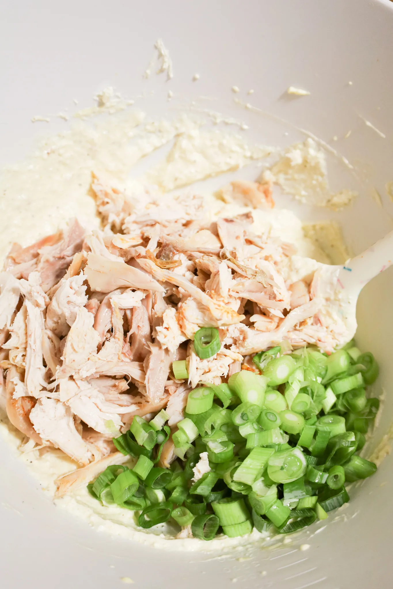 chopped green onions and shredded chicken on top of a creamy mixture in a mixing bowl