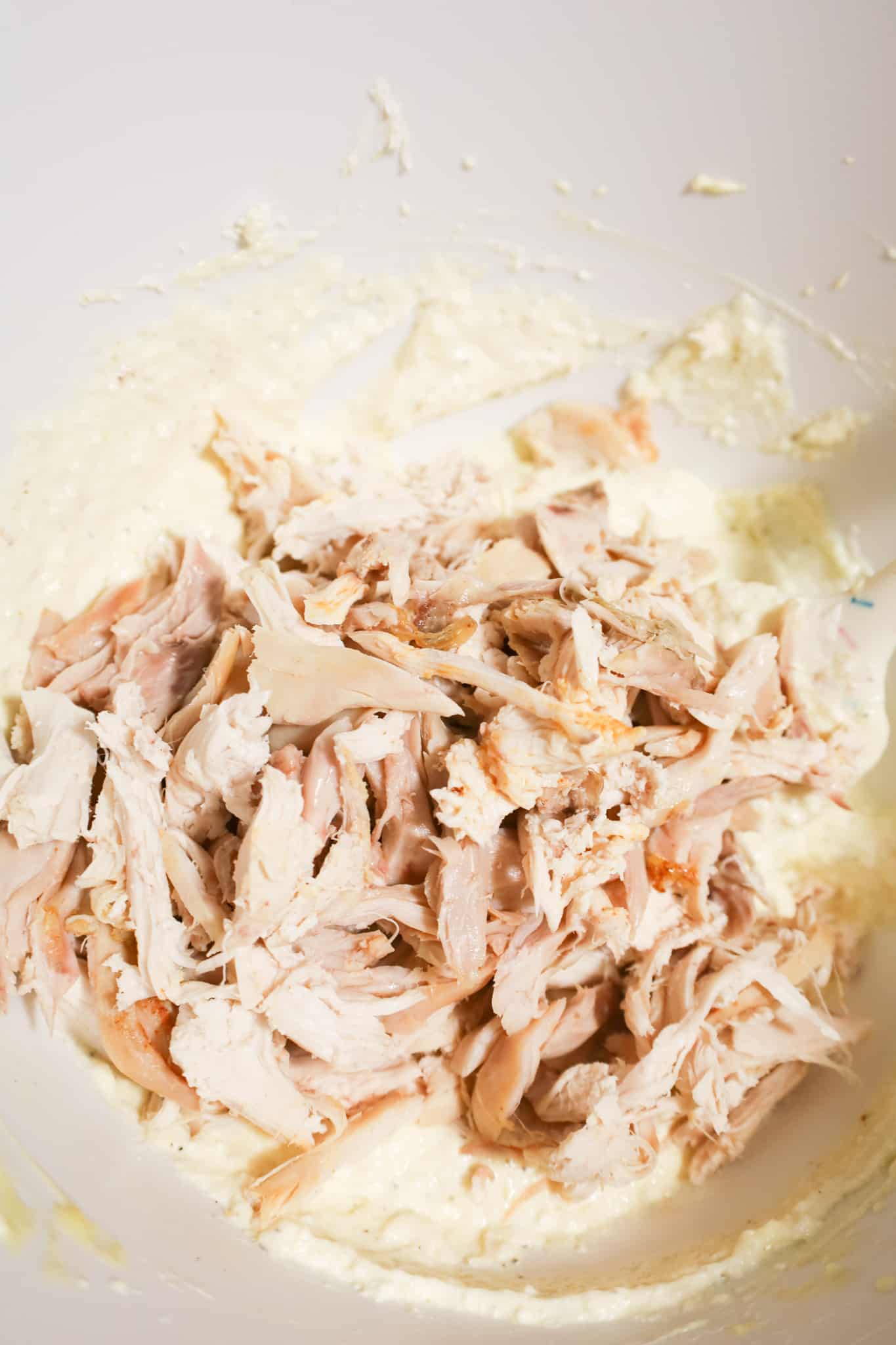 shredded chicken on top of creamy mixture in a mixing bowl