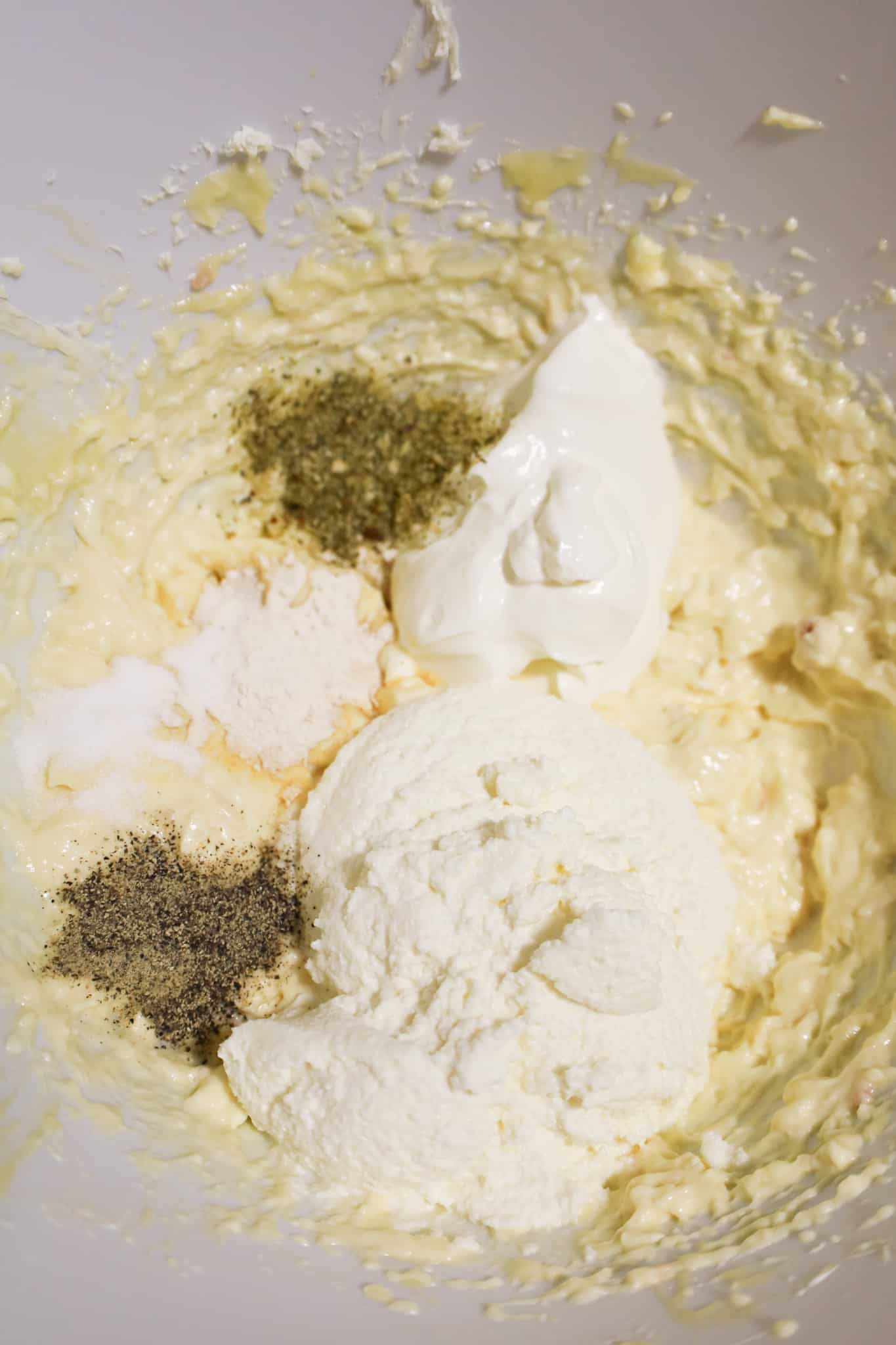 ricotta cheese, sour cream and spices on top of a cream cheese mixture in a mixing bowl