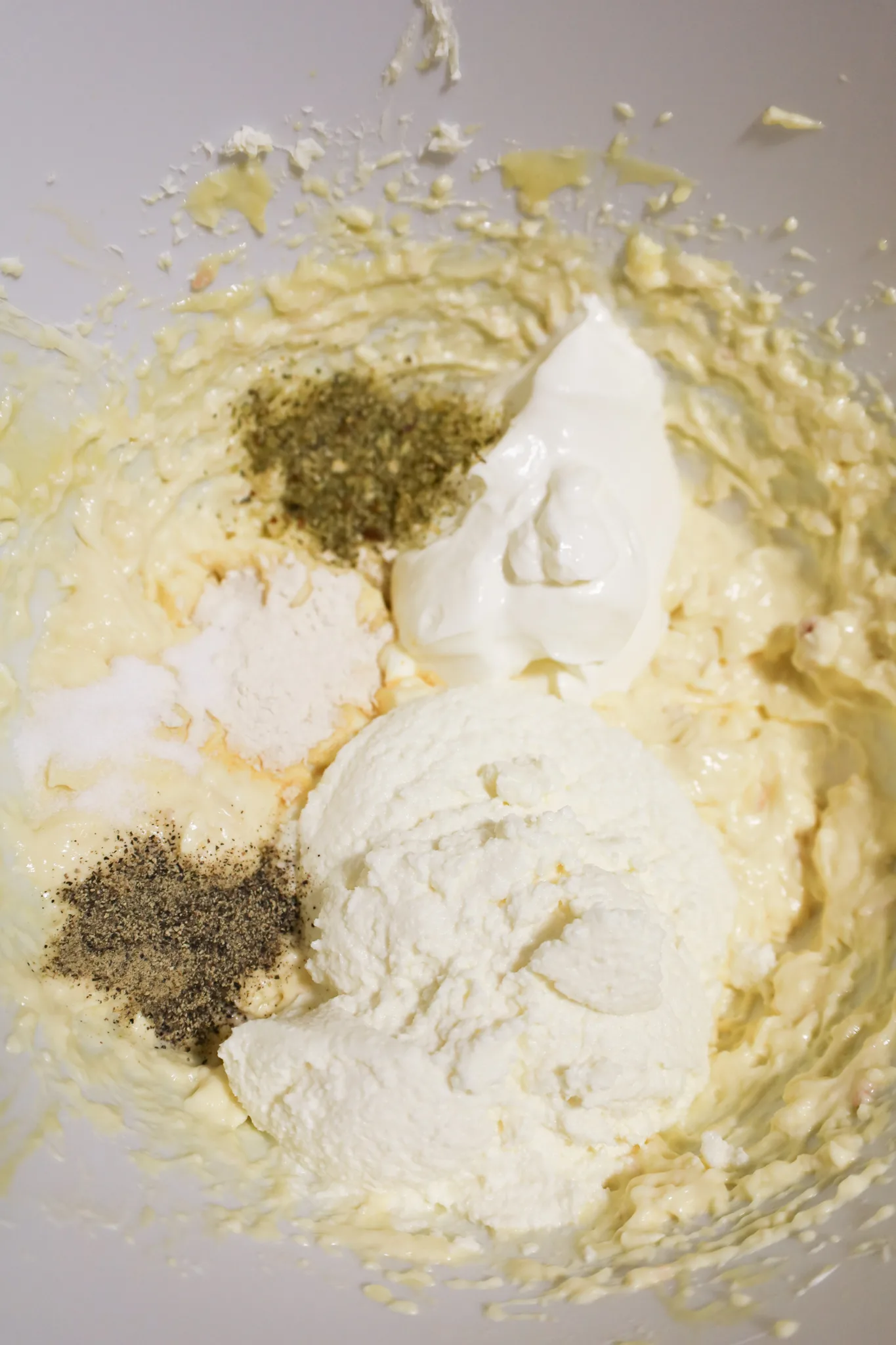ricotta cheese, sour cream and spices on top of a cream cheese mixture in a mixing bowl