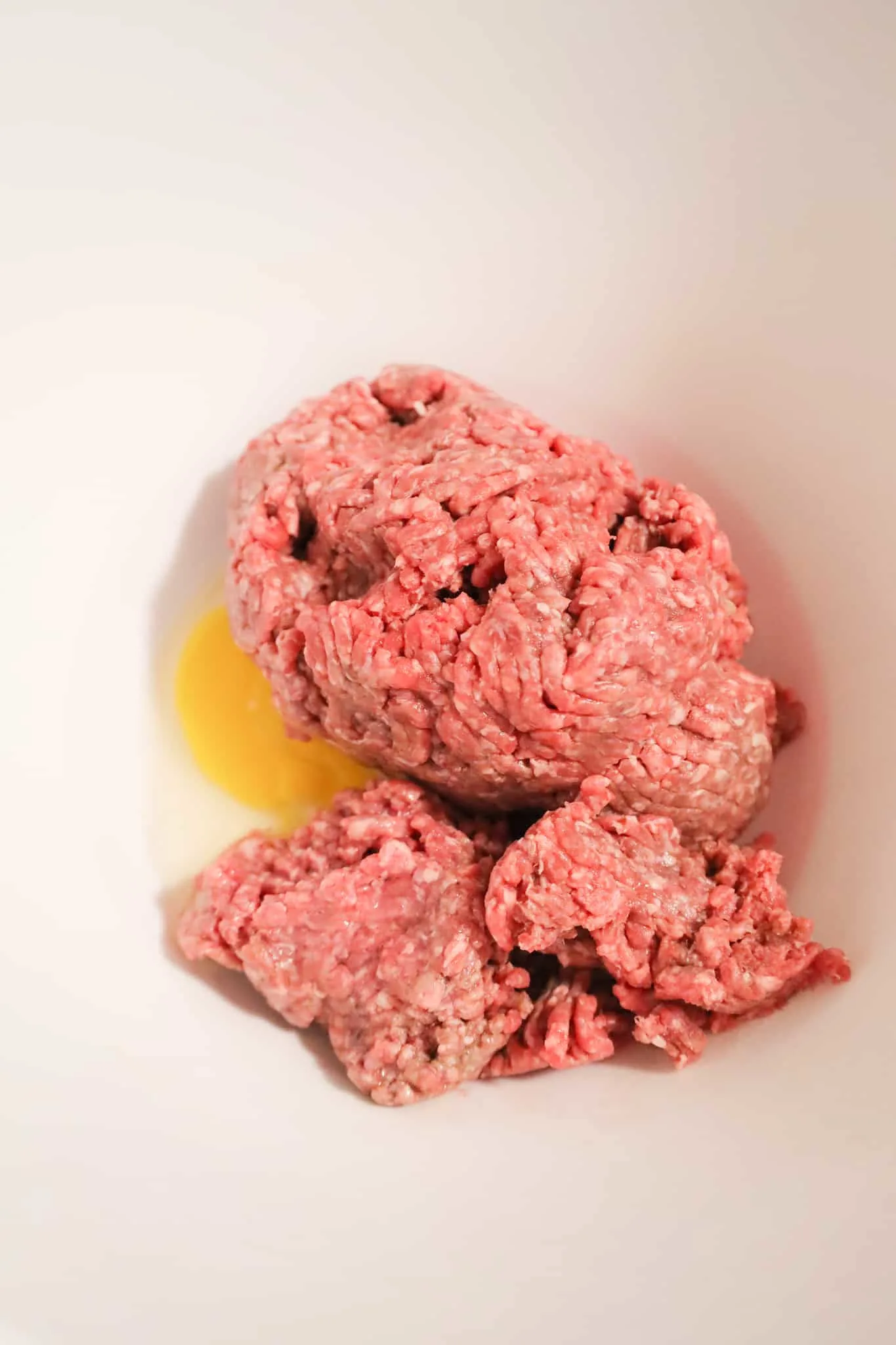 raw ground beef and raw egg in a mixing bowl