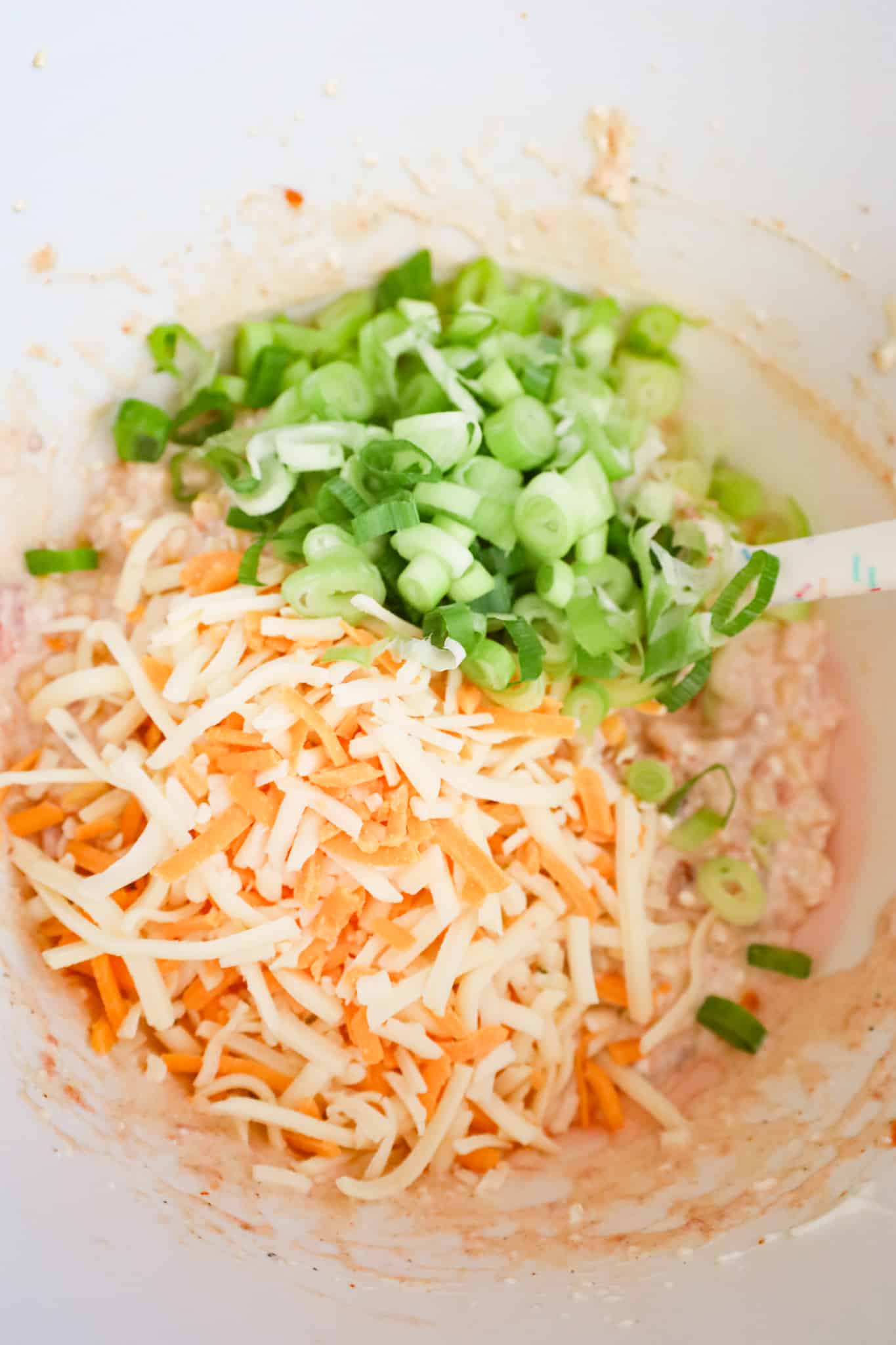 chopped green onions and shredded cheese on top of cream cheese and corn mixture in a mixing bowl