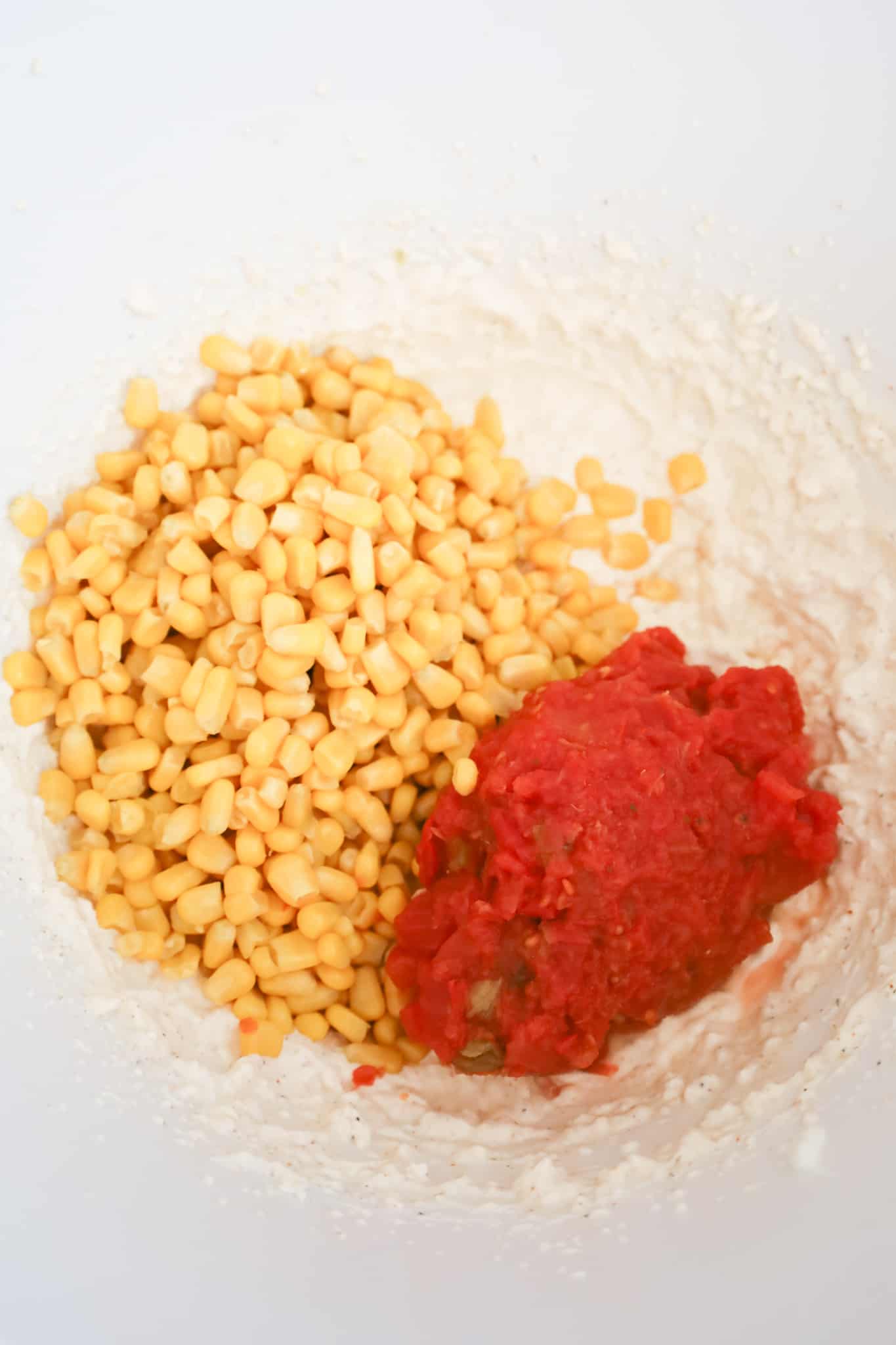 canned corn and Rotel on top of cream cheese mixture in a mixing bowl