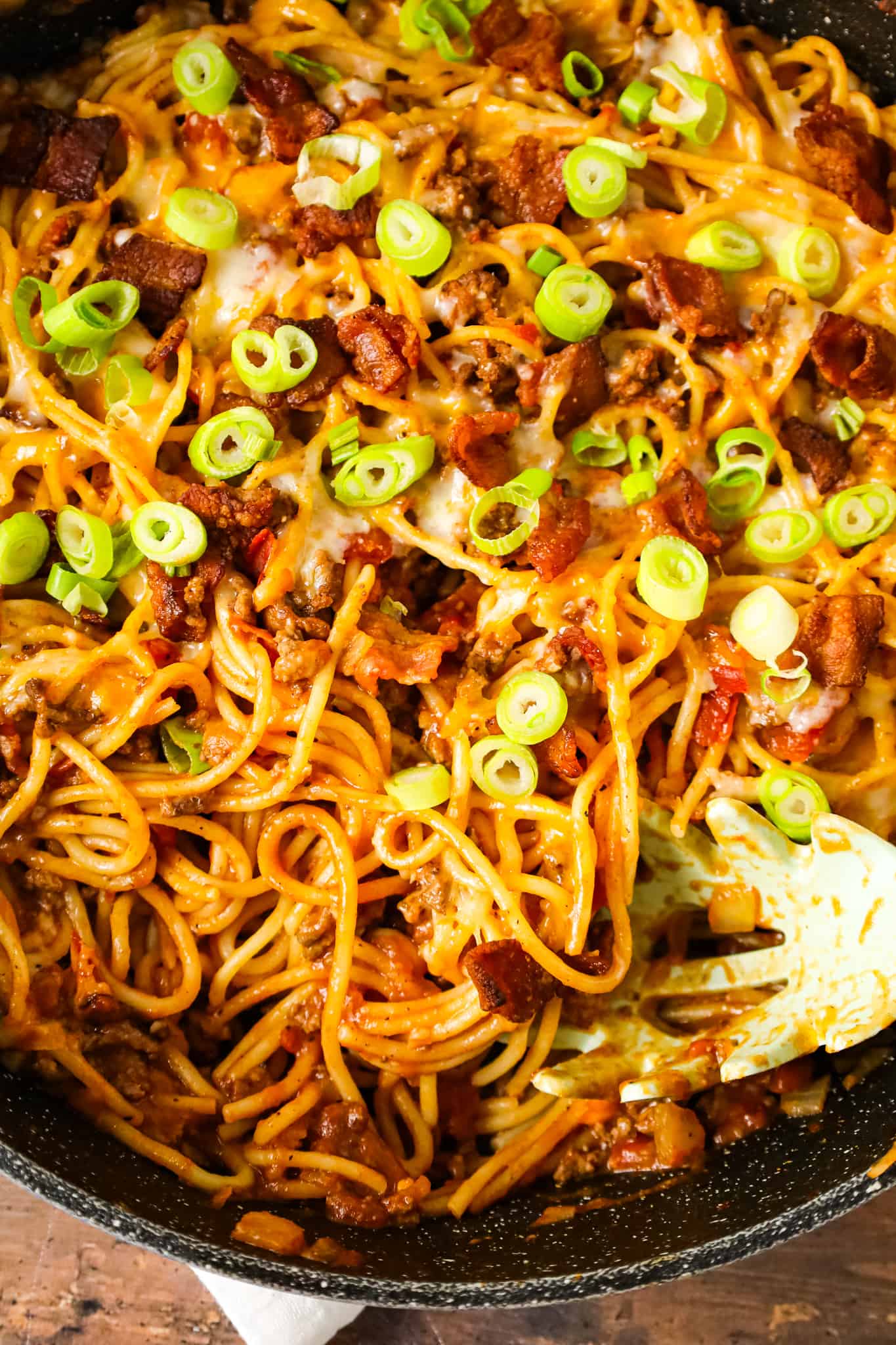 Cowboy Spaghetti is a hearty pasta recipe loaded with bacon, ground beef, Rotel diced tomatoes and green chilies, tomato sauce, bbq sauce, shredded cheese and chopped green onions.