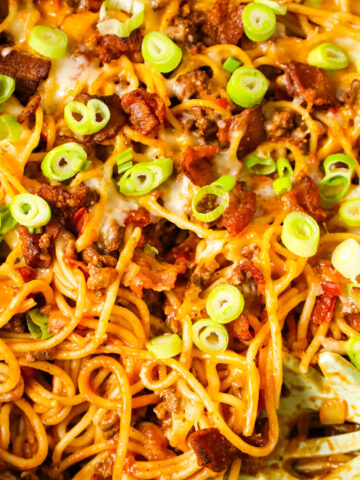 Cowboy Spaghetti is a hearty pasta recipe loaded with bacon, ground beef, Rotel diced tomatoes and green chilies, tomato sauce, bbq sauce, shredded cheese and chopped green onions.