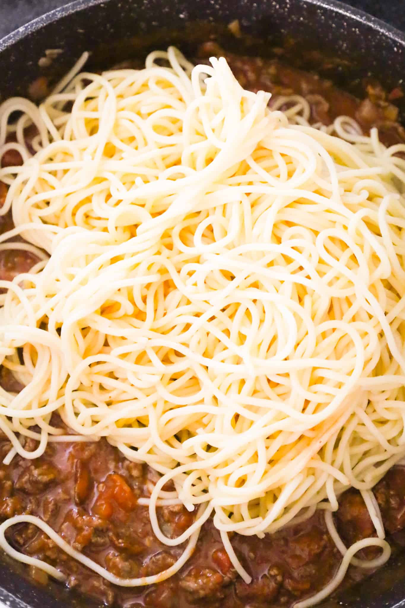 cooked spaghetti on top of ground beef mixture in a skillet