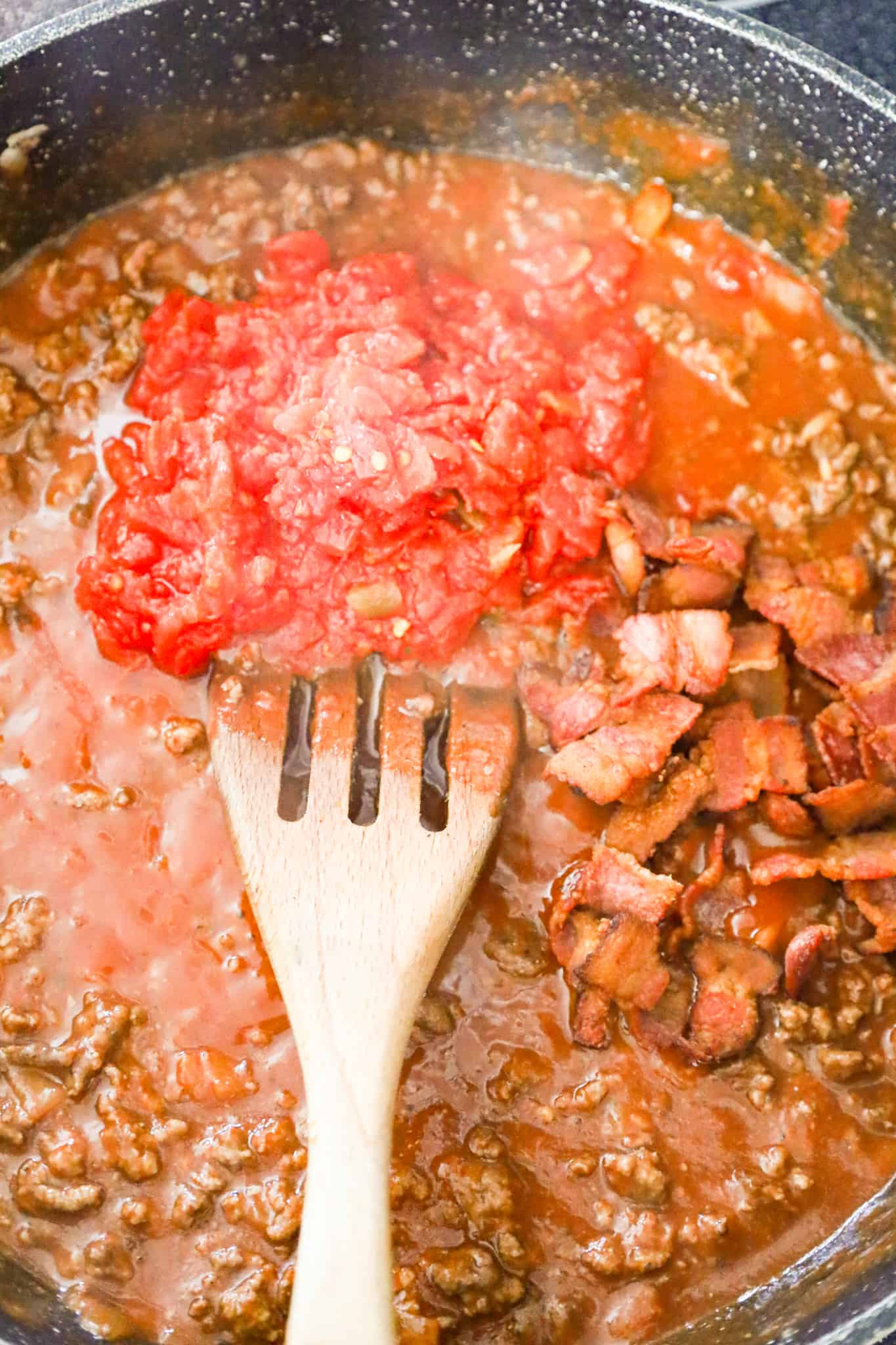 Rotel and cooked bacon pieces on top of ground beef and sauce mixture in a skillet