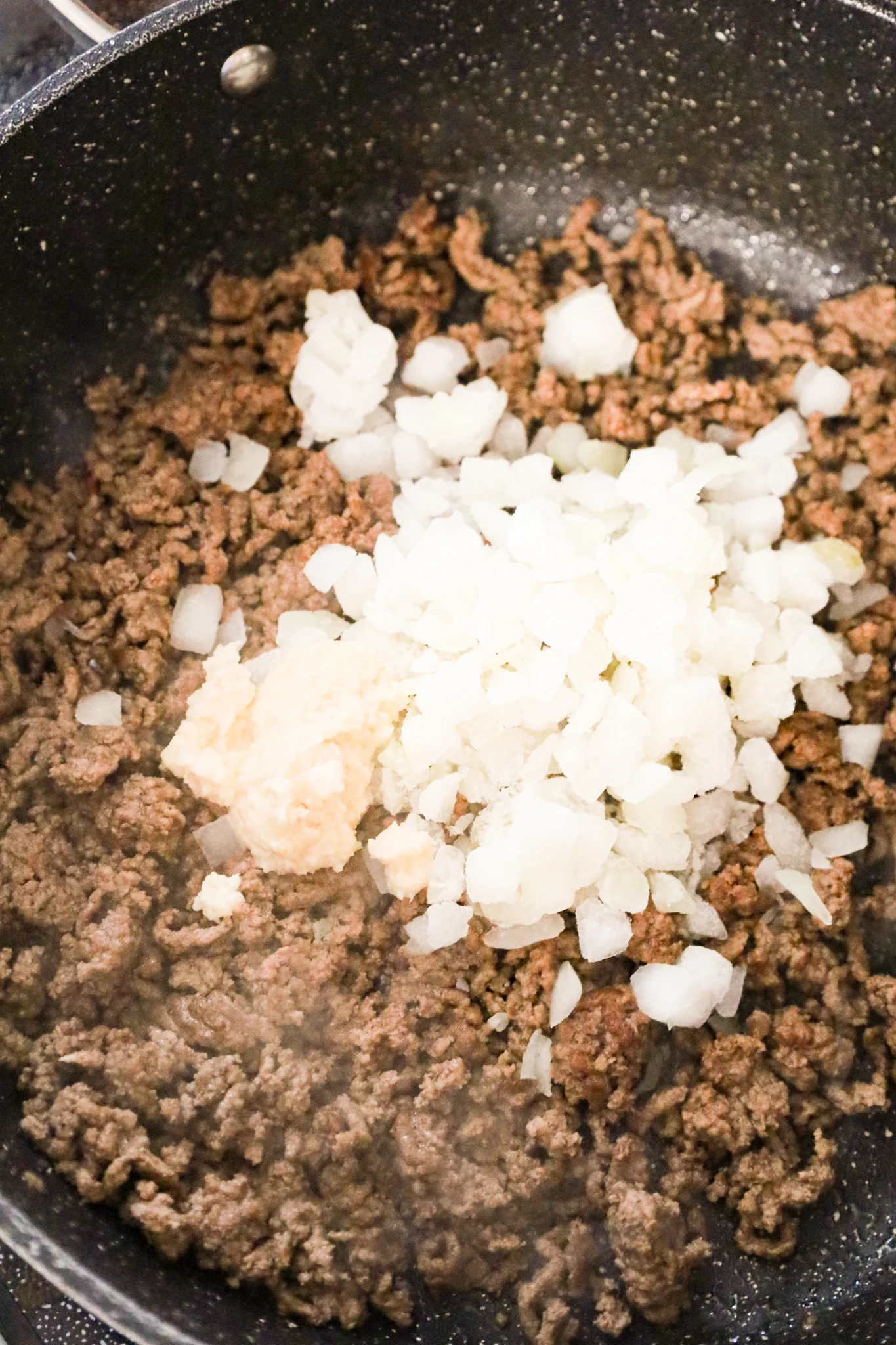 garlic puree and diced onion on top of cooked ground beef in a skillet