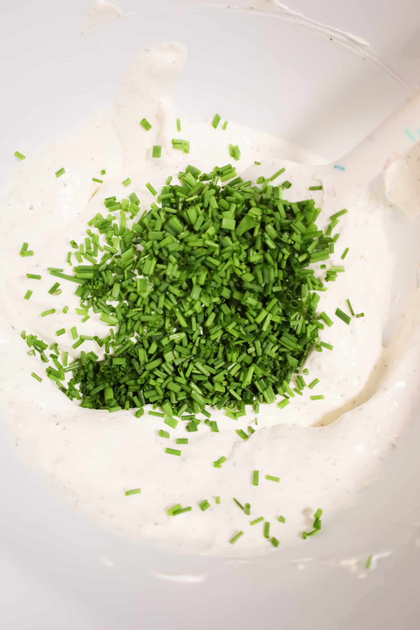 chopped chives on top of sour cream in a mixing bowl