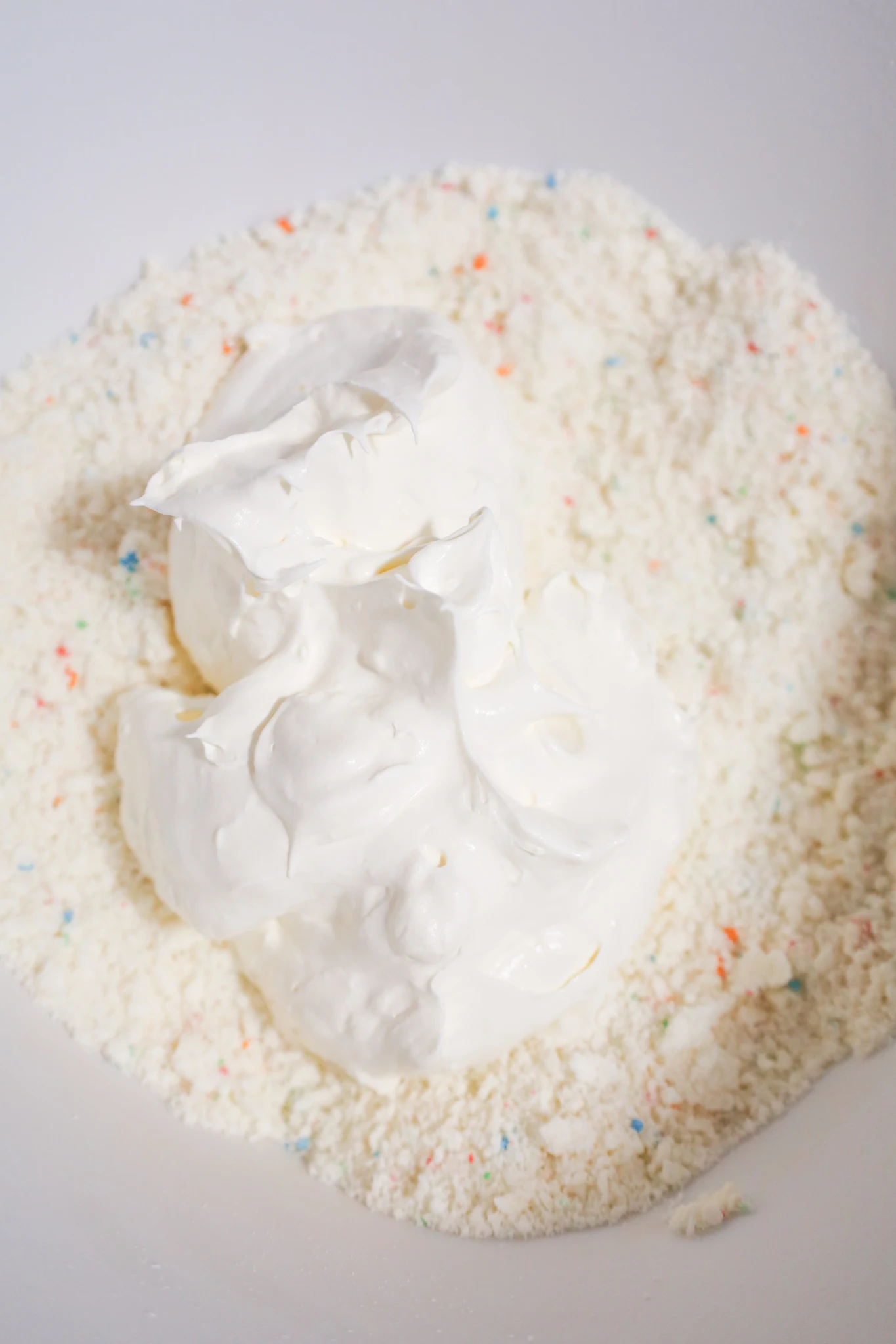 Cool Whip on top of funfetti cake mixture in a mixing bowl