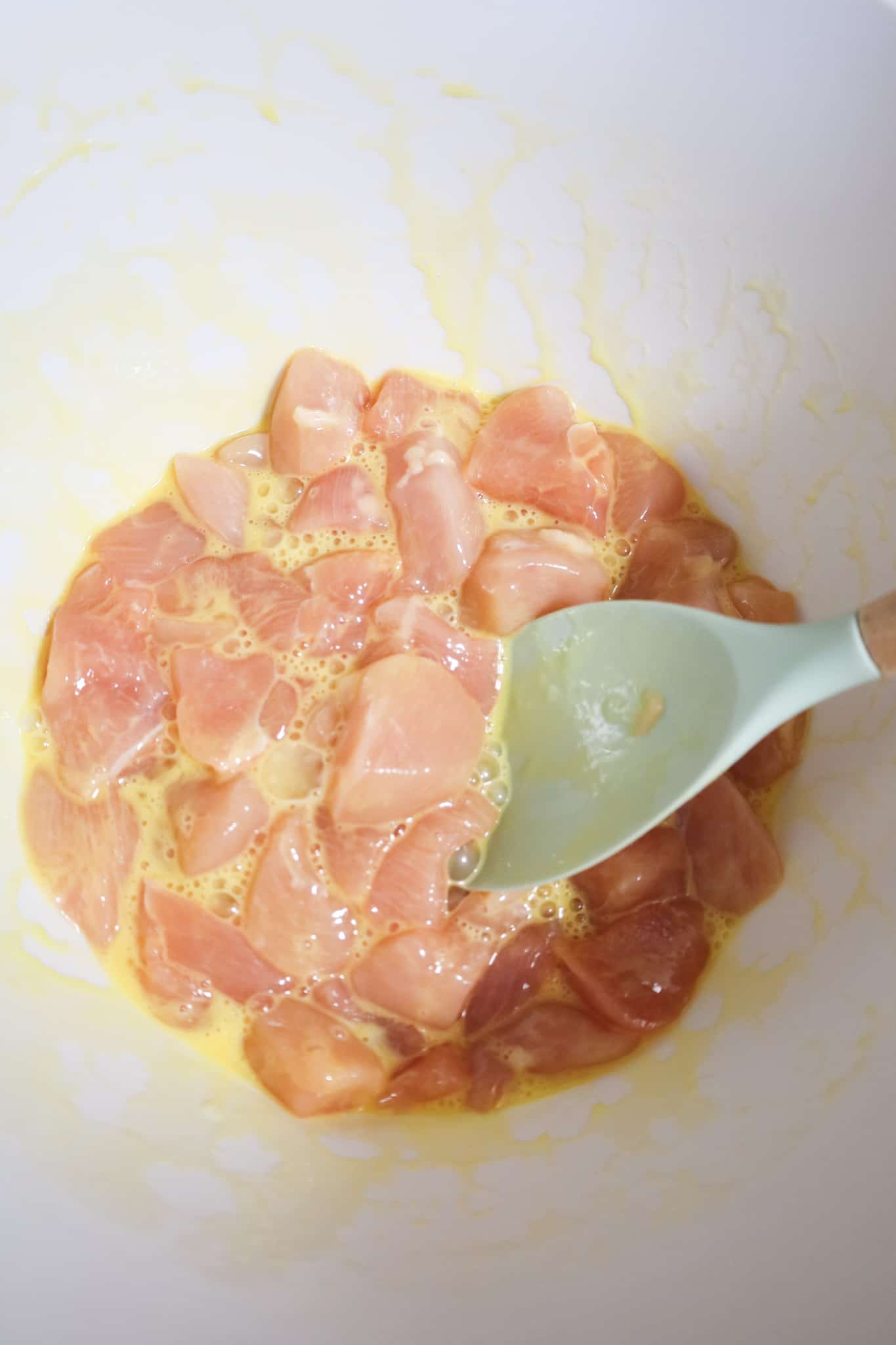chicken breast chunks coated in egg in a mixing bowl