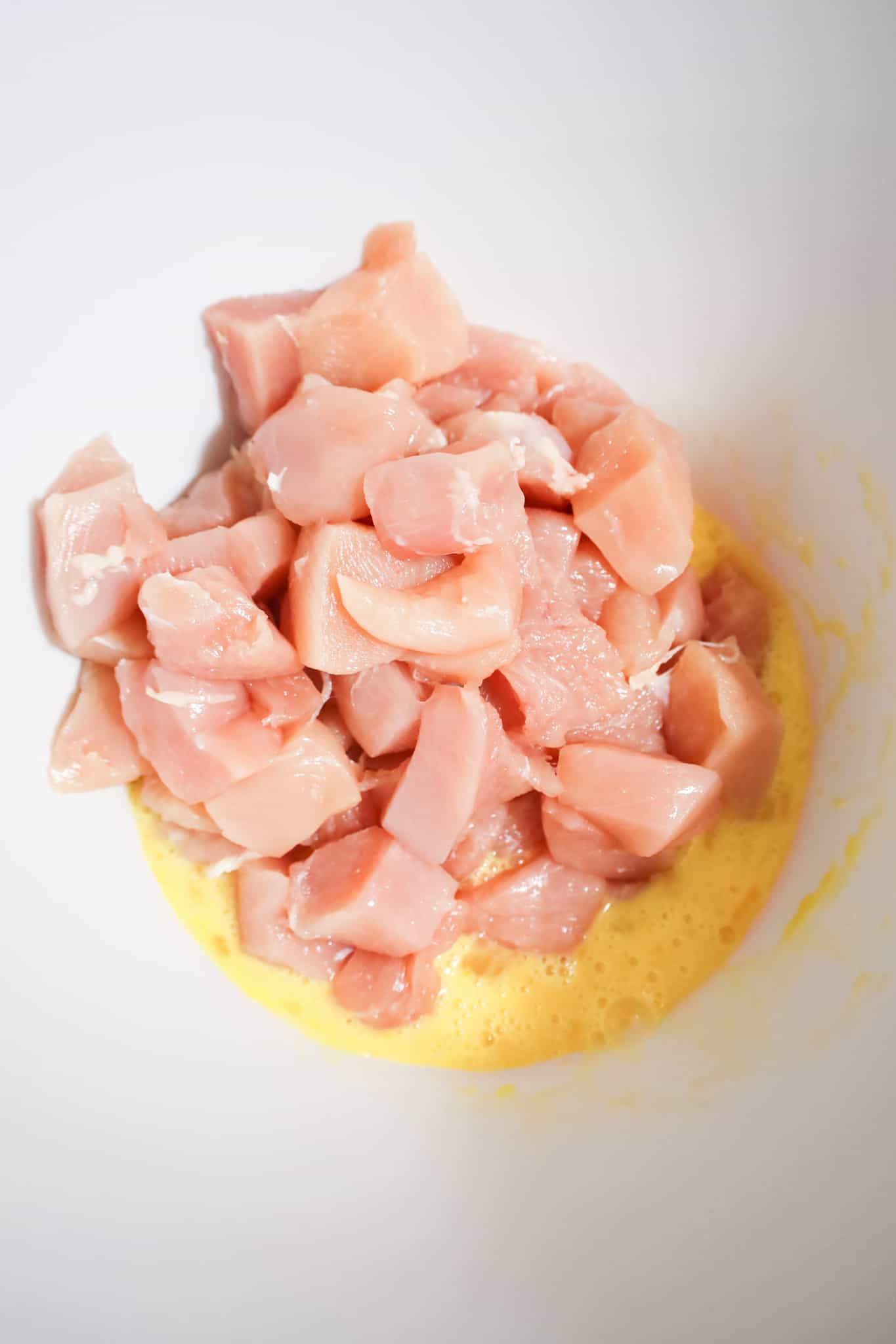 raw chicken breast chunks on top of beaten eggs in a mixing bowl