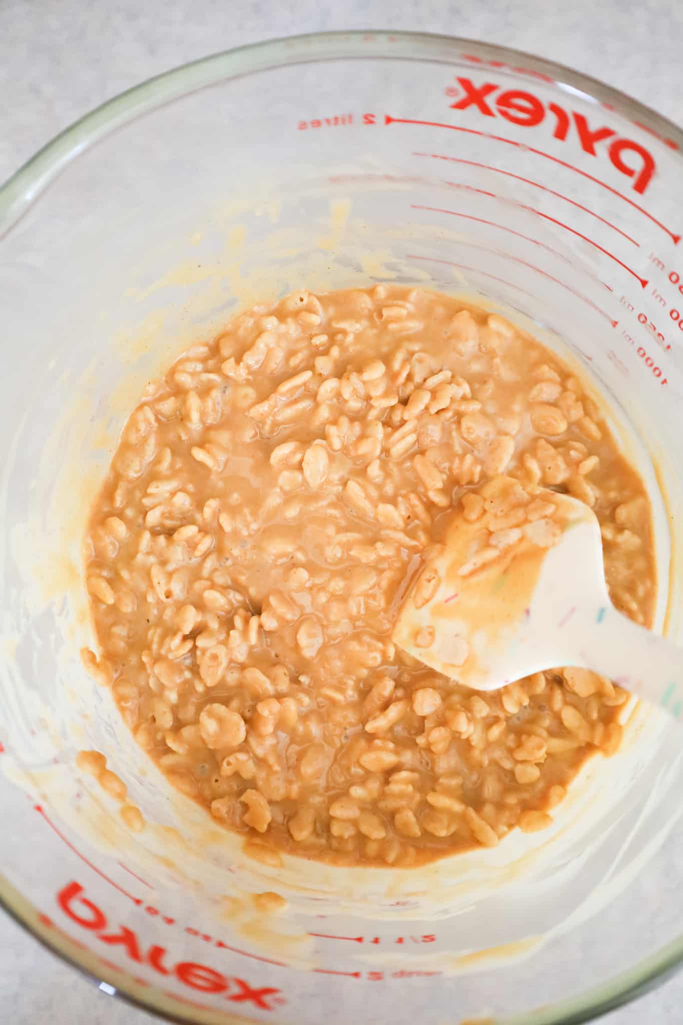 rice krispies being stirred into a melted peanut butter mixture in a glass bowl