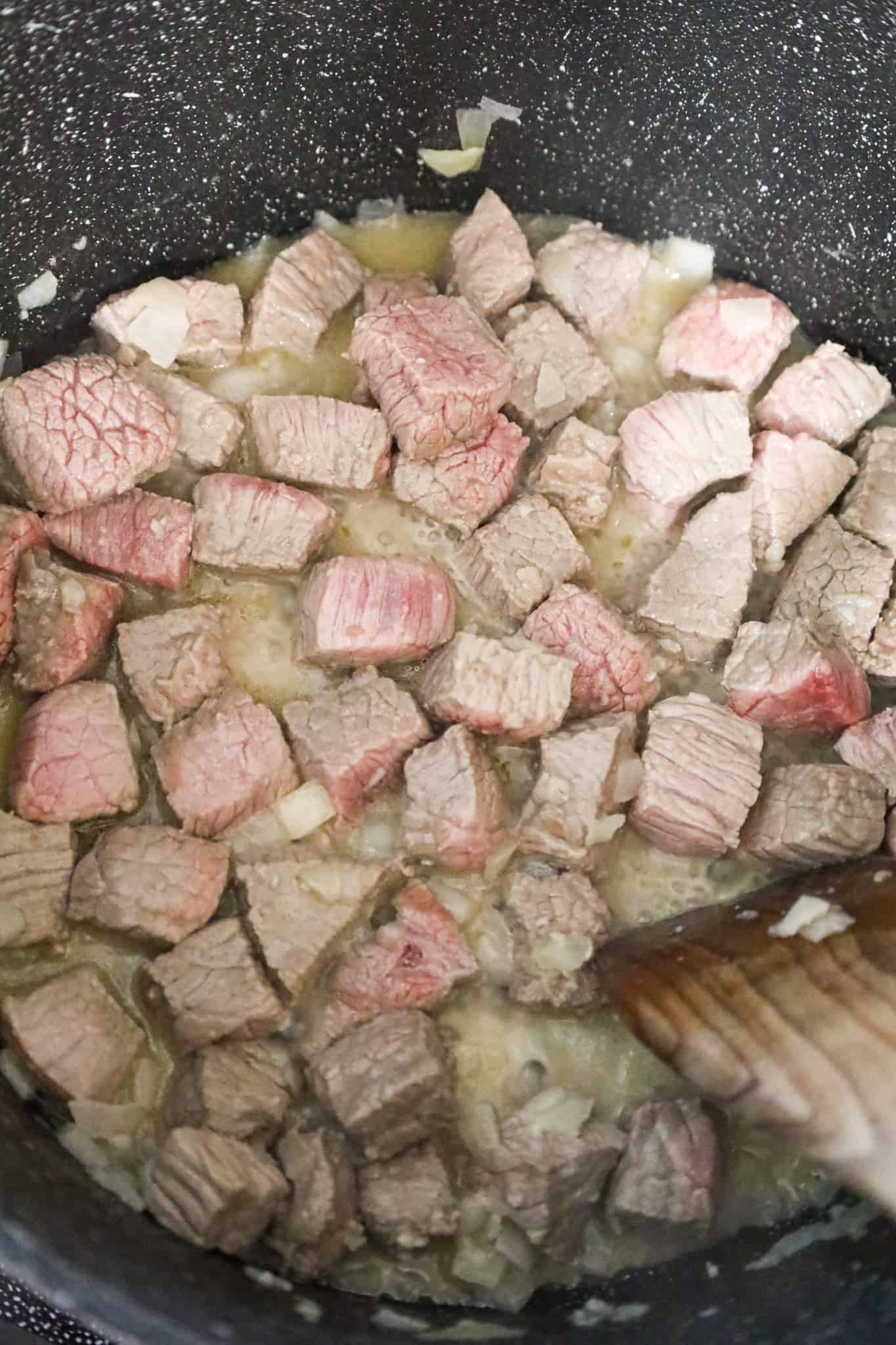 steak chunks cooking a large pot with butter