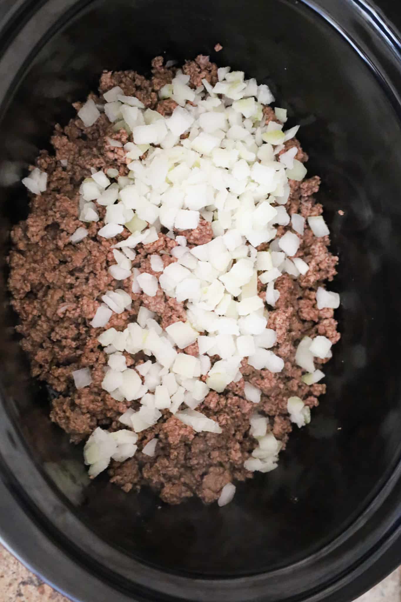 diced onions on top of cooked ground beef in a crock pot
