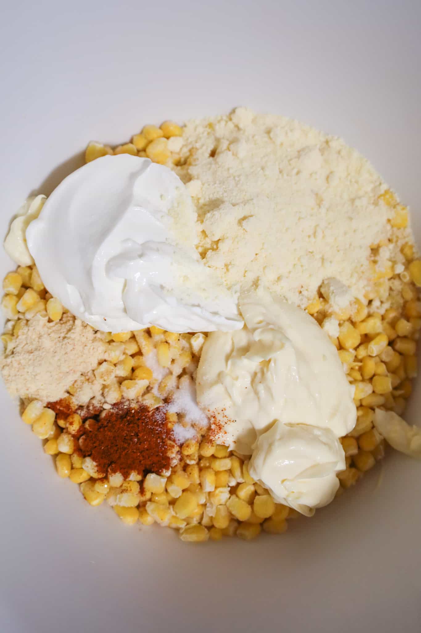 grated parmesan, sour cream, mayo and chili powder on top of frozen corn in a mixing bowl
