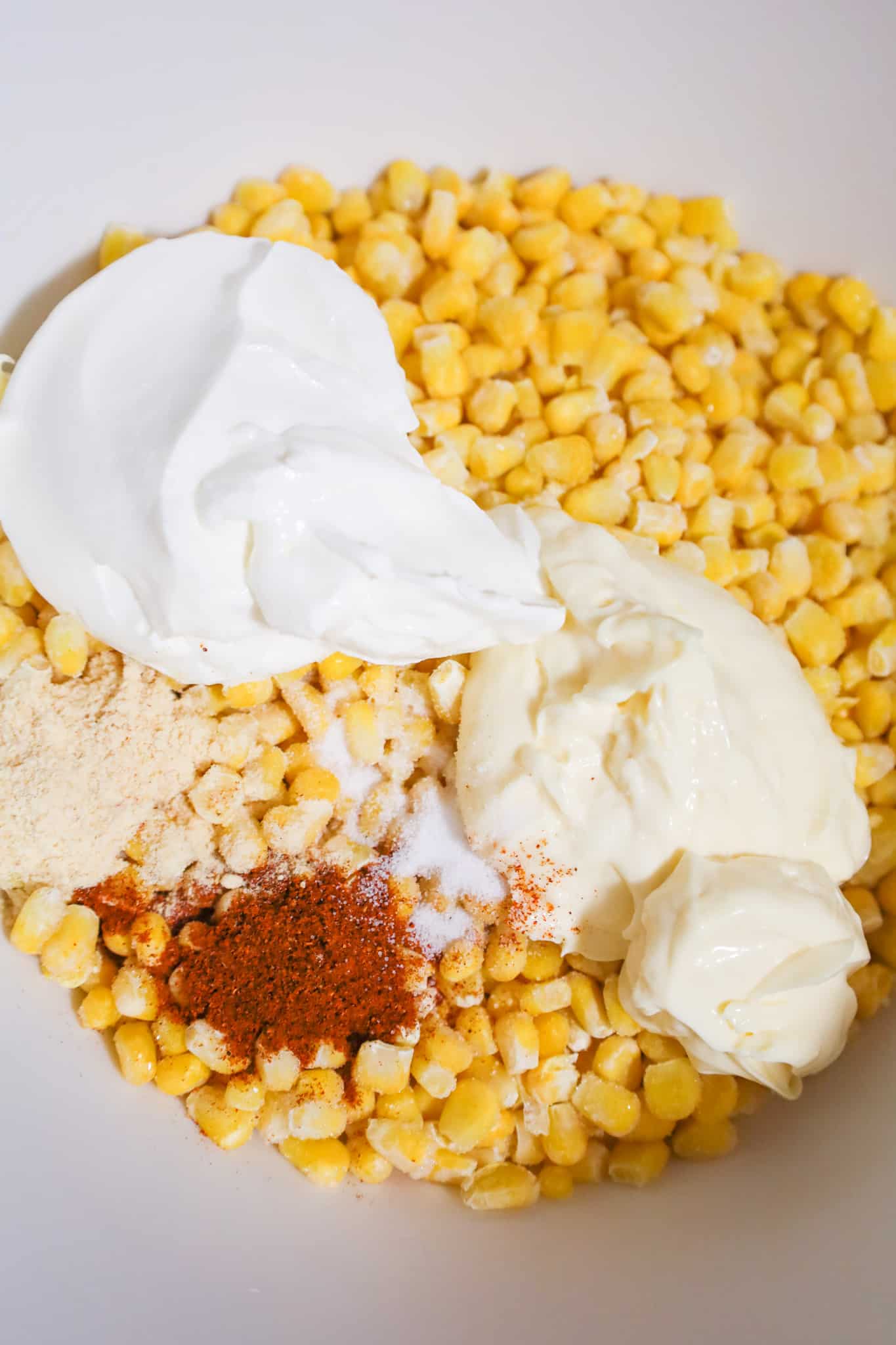 chili powder, garlic powder, mayo and sour cream on top of corn kernels in a mixing bowl