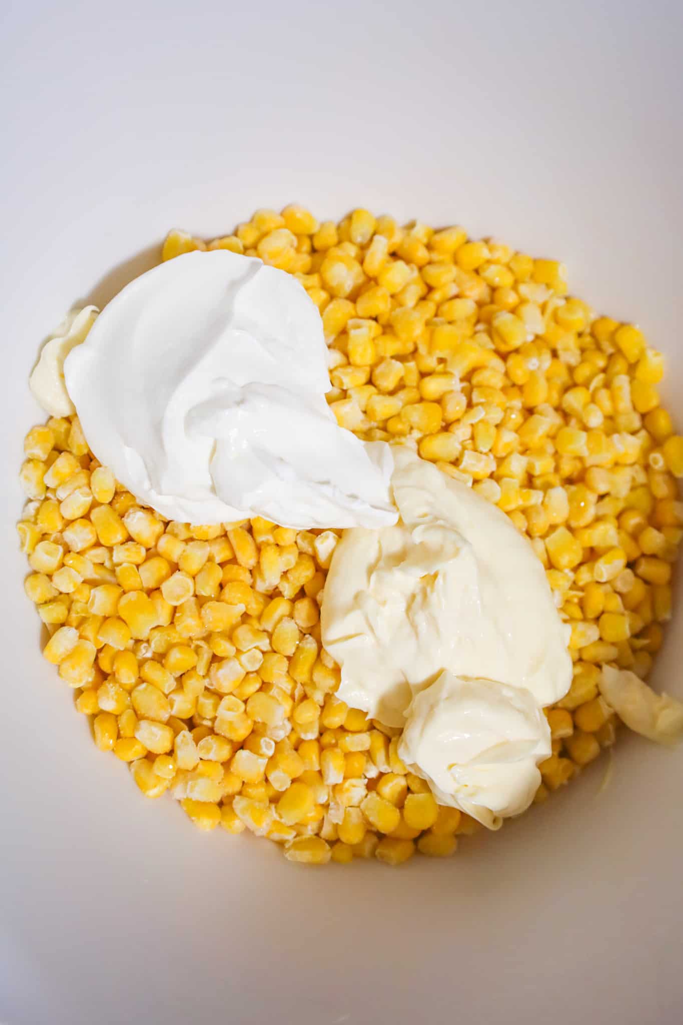 sour cream and mayo on top of frozen corn in a mixing bowl