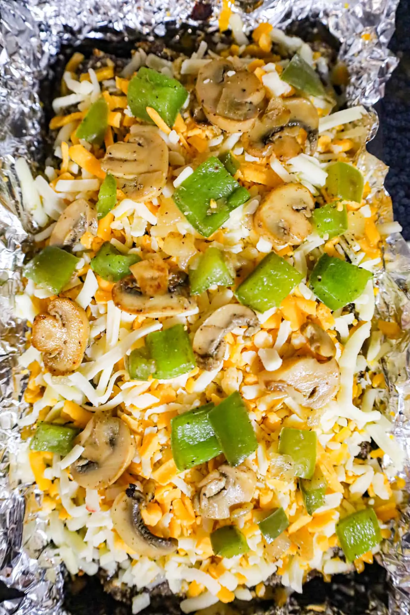diced green peppers and sliced mushrooms on top of shredded cheese