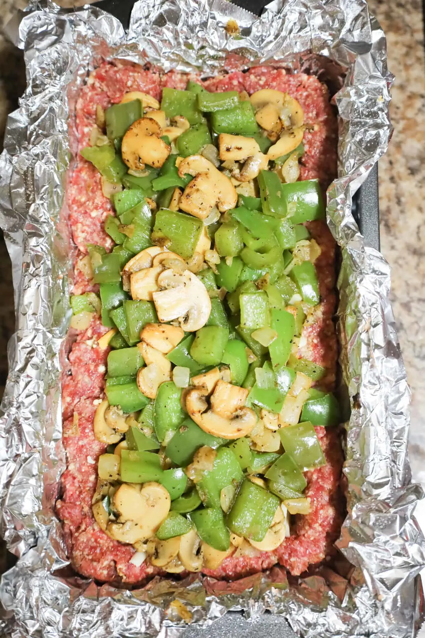diced green peppers and sliced mushrooms on top of ground beef mixture in a loaf pan