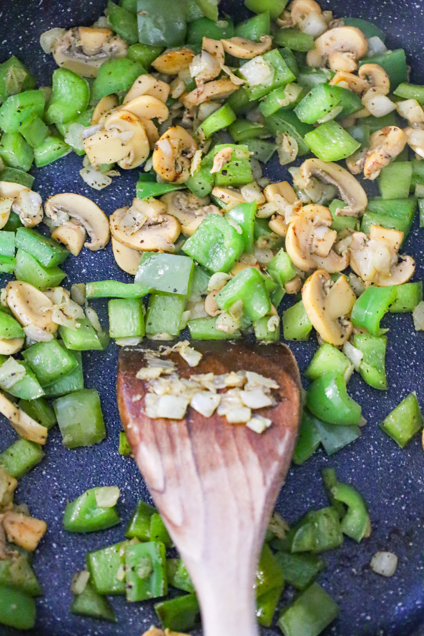 sliced mushrooms, diced green peppers and onions cooking in a skillet