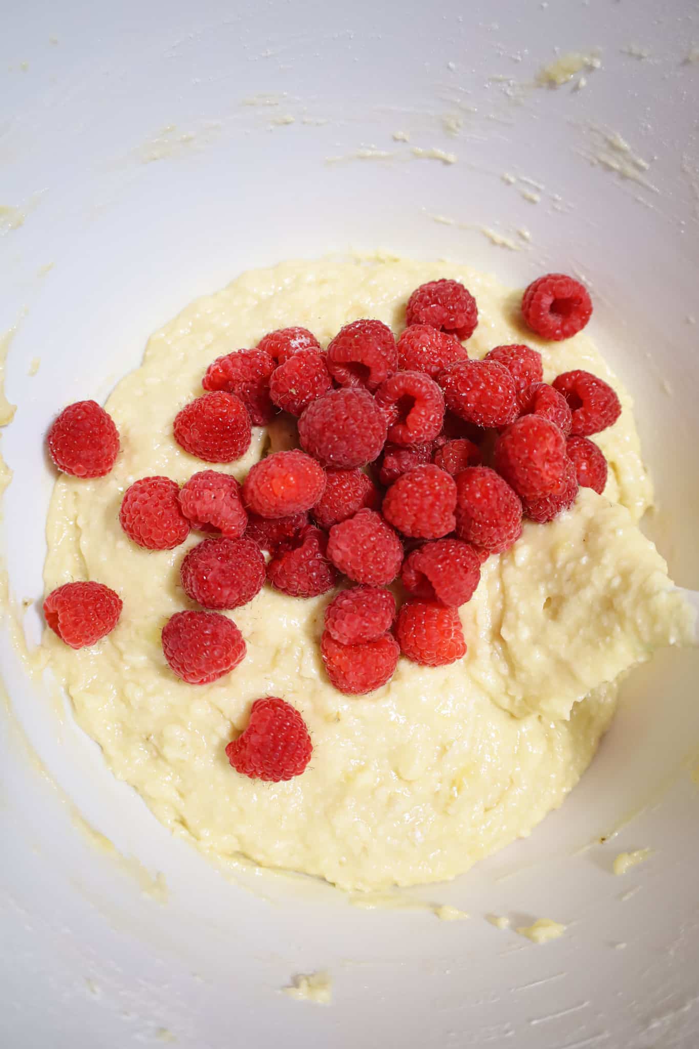 fresh raspberries on top of banana bread batter in a mixing bowl