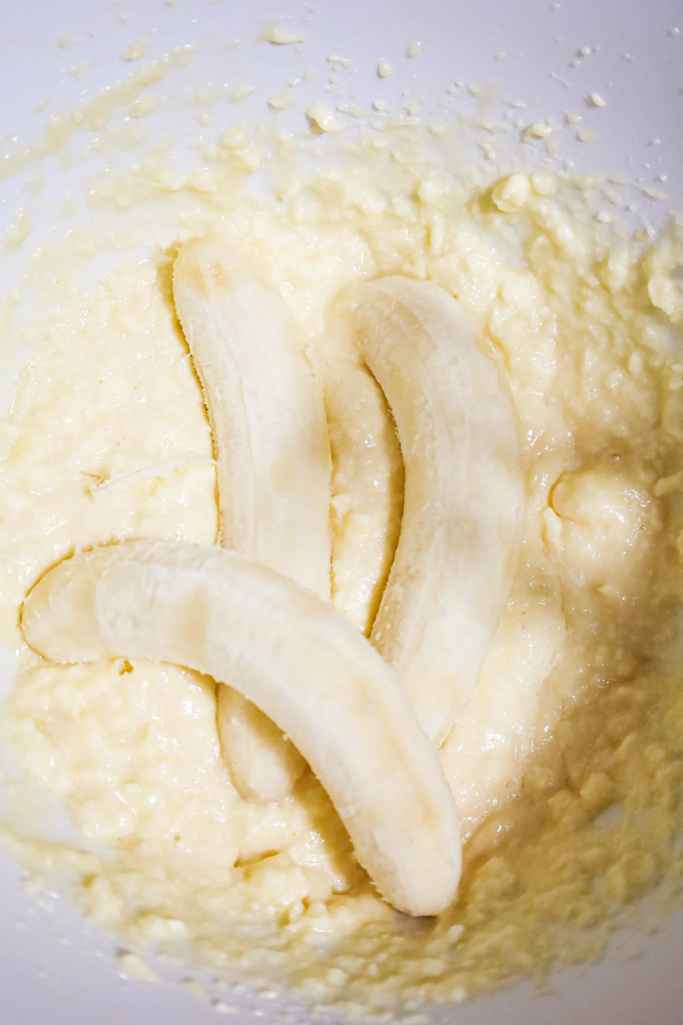 ripe bananas on top of butter, egg and sugar mixture in a mixing bowl