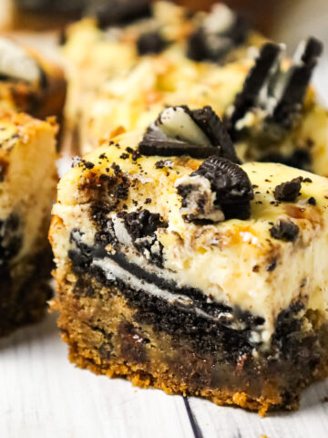 Slutty Cheesecake Bars are a decadent dessert recipe with a base of chocolate chip cookie dough topped with Oreo cookies, cheesecake and Skor toffee bits.