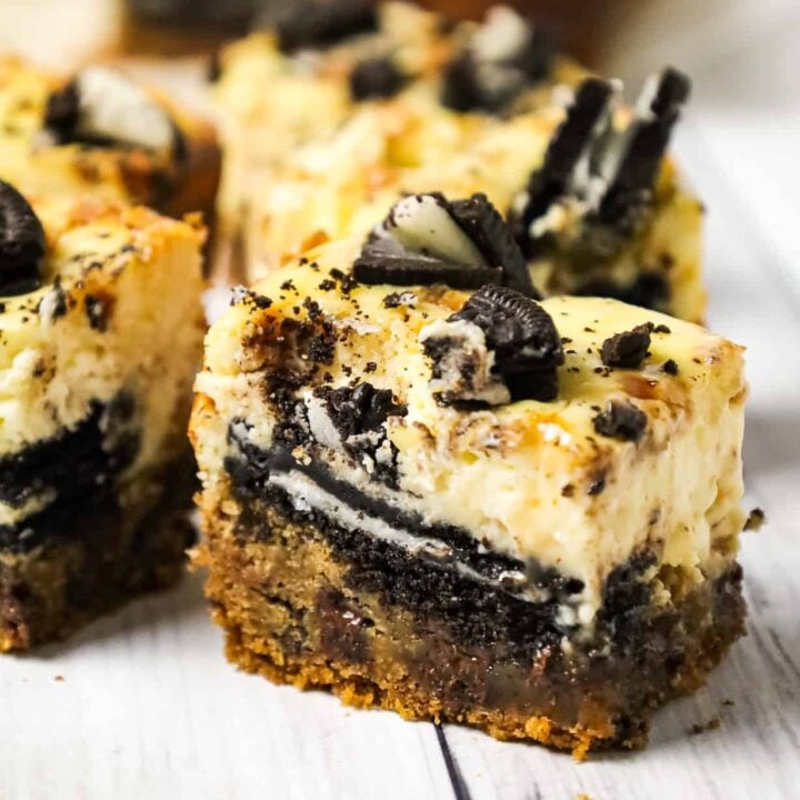 Slutty Cheesecake Bars are a decadent dessert recipe with a base of chocolate chip cookie dough topped with Oreo cookies, cheesecake and Skor toffee bits.