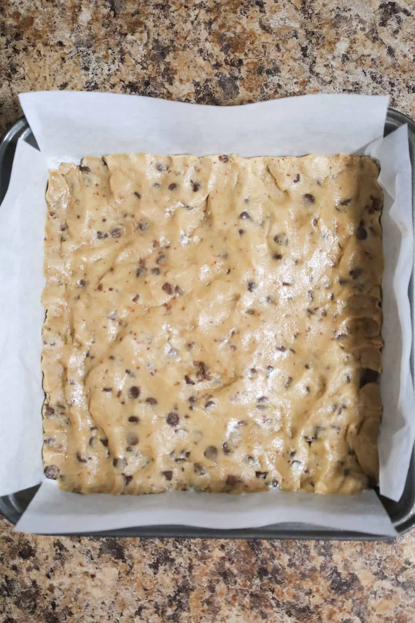 chocolate chip cookie dough pressed into bottom of parchment lined baking dish