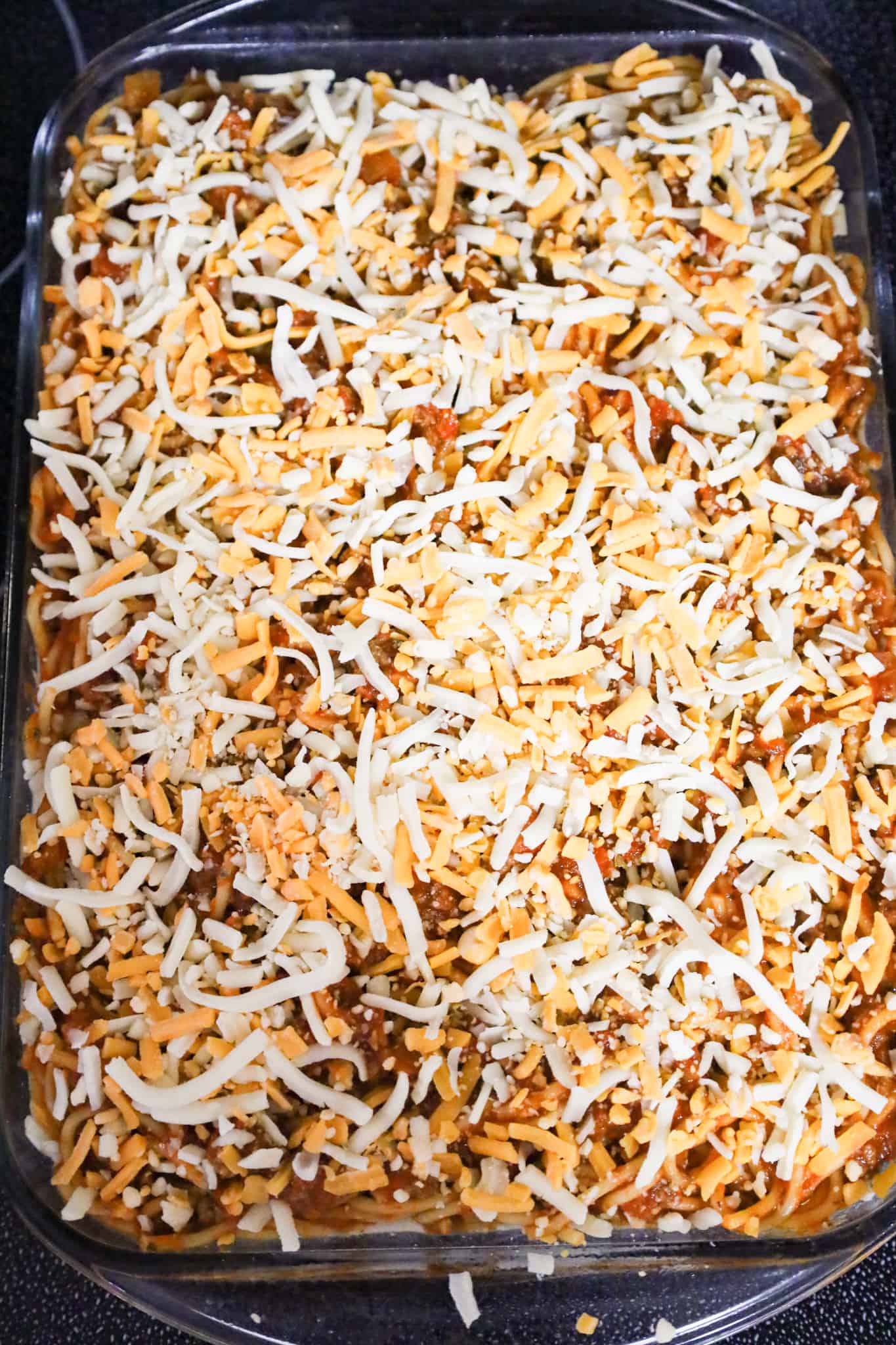 shredded mozzarella and cheddar cheese on top of spaghetti in a baking dish