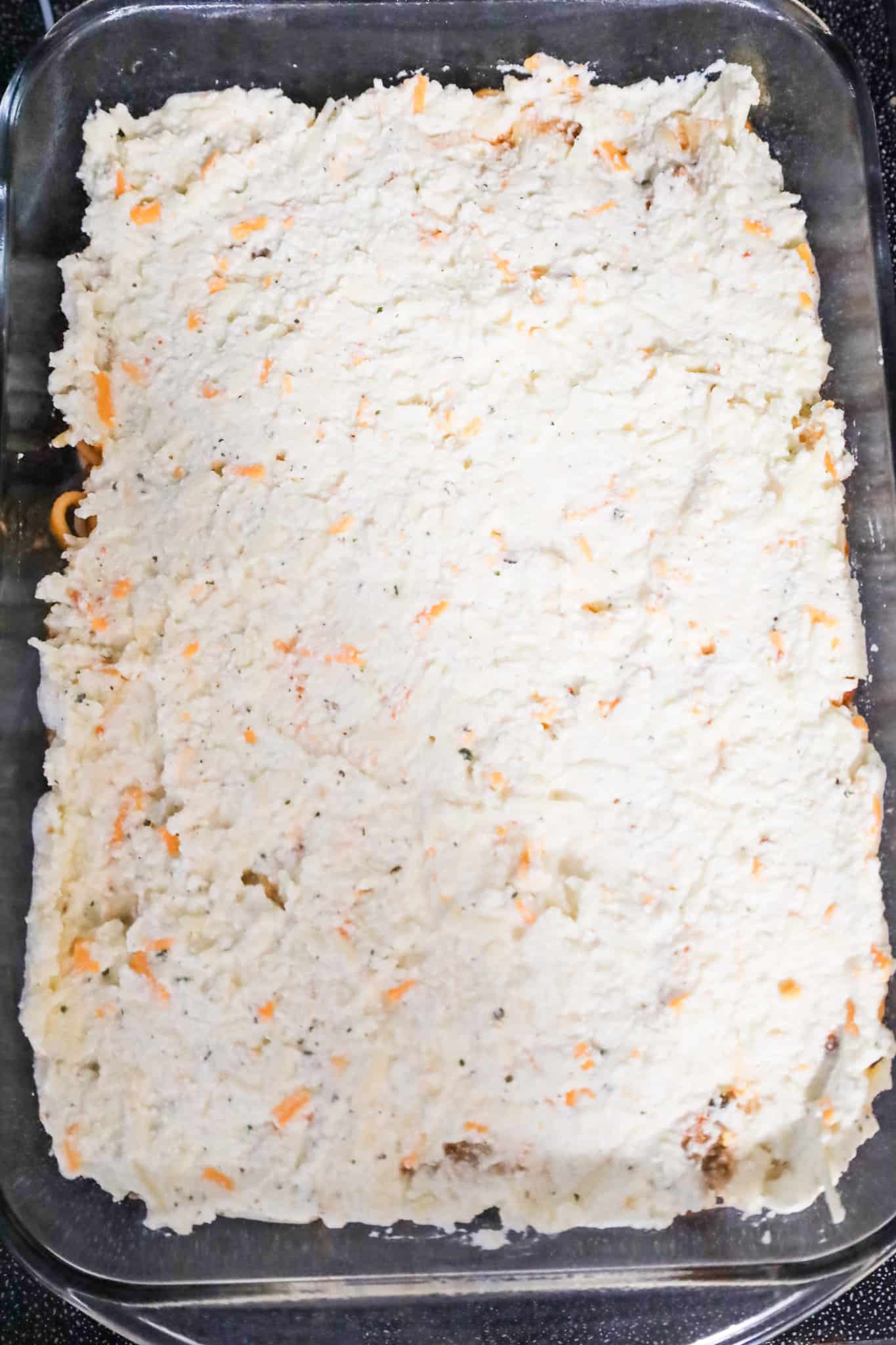 ricotta and shredded cheese mixture on top of spaghetti in a baking dish