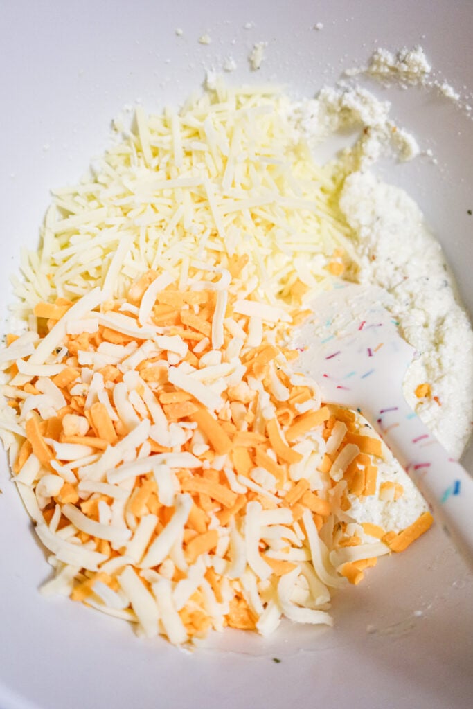 shredded parmesan, cheddar and mozzarella on top of ricotta in a mixing bowl