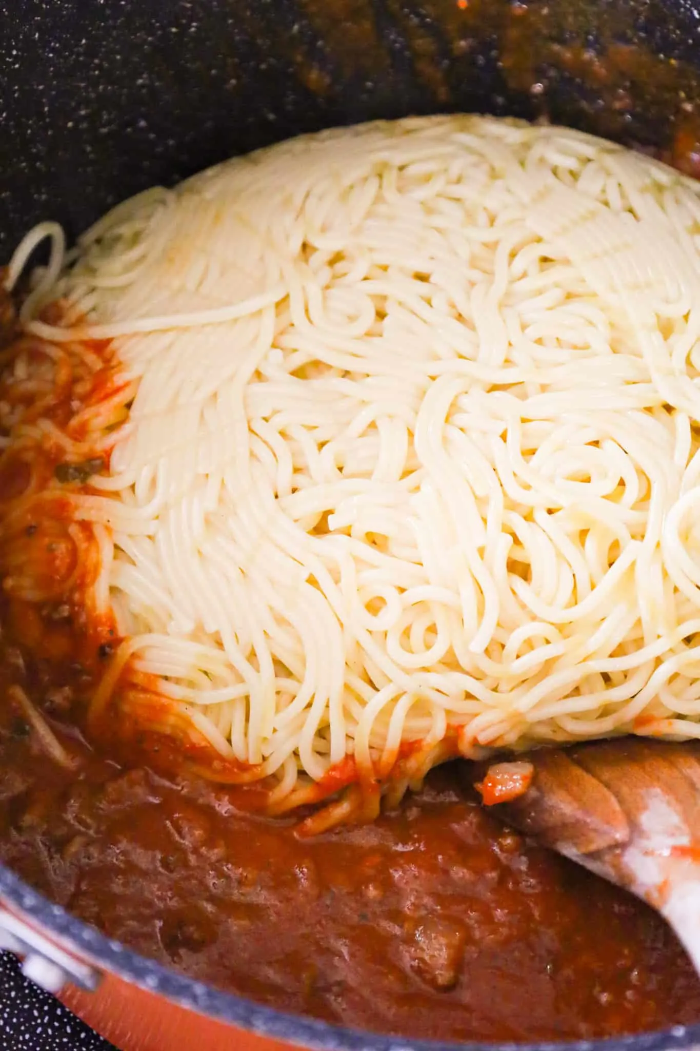 cooked spaghetti on top of marinara and ground beef mixture in a large pot
