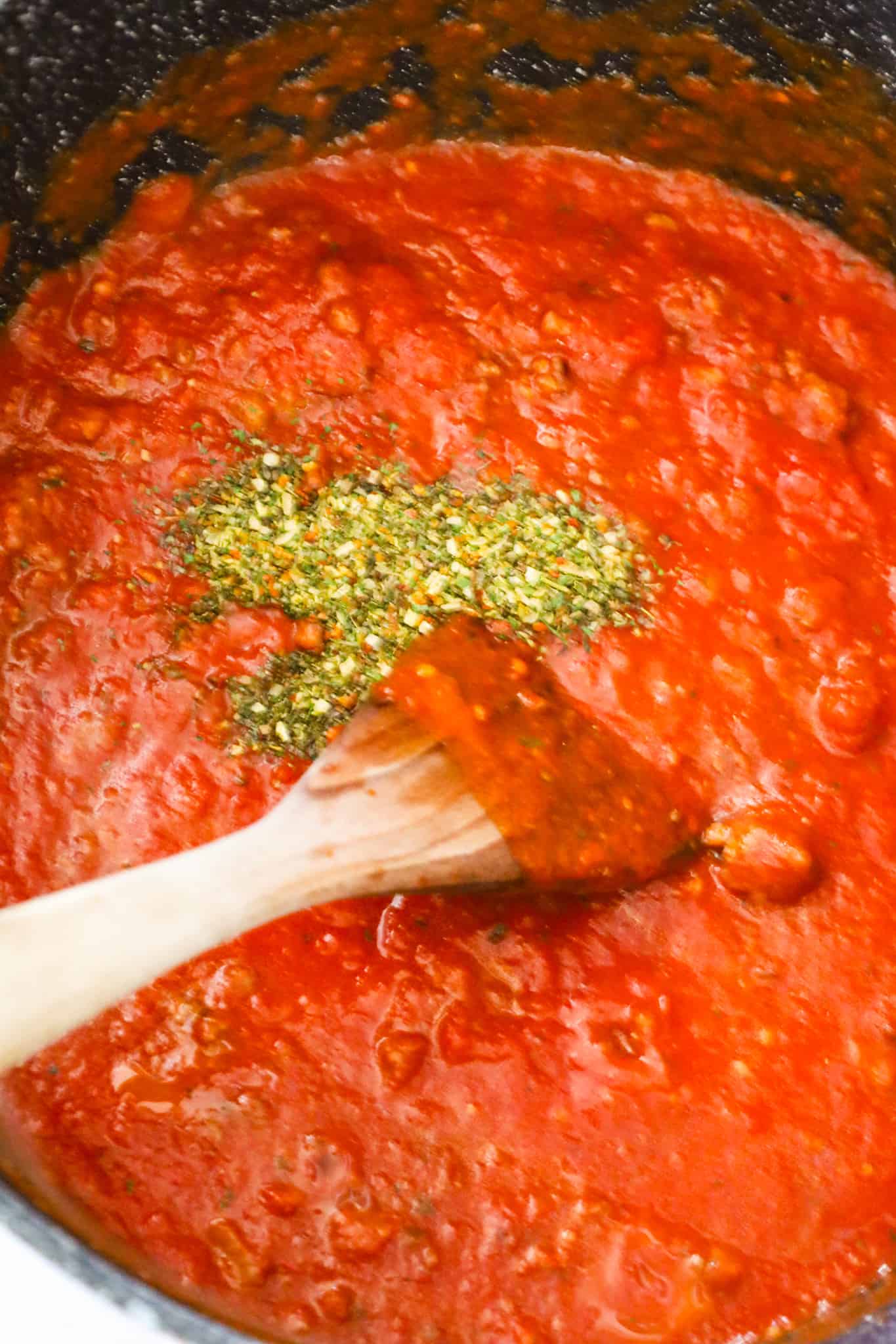 Italian seasoning on top of marinara sauce in a large pot