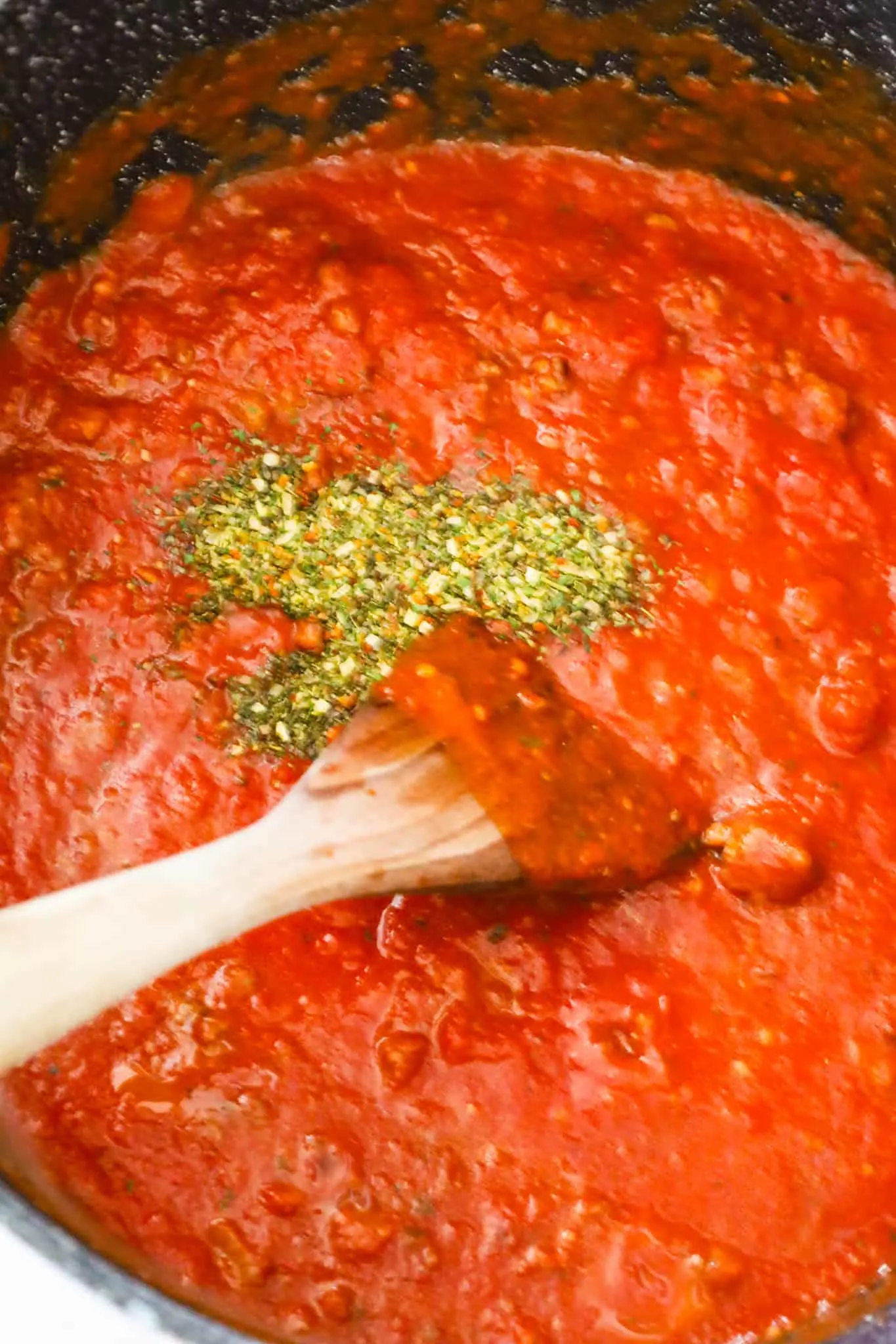 Italian seasoning on top of marinara sauce in a large pot