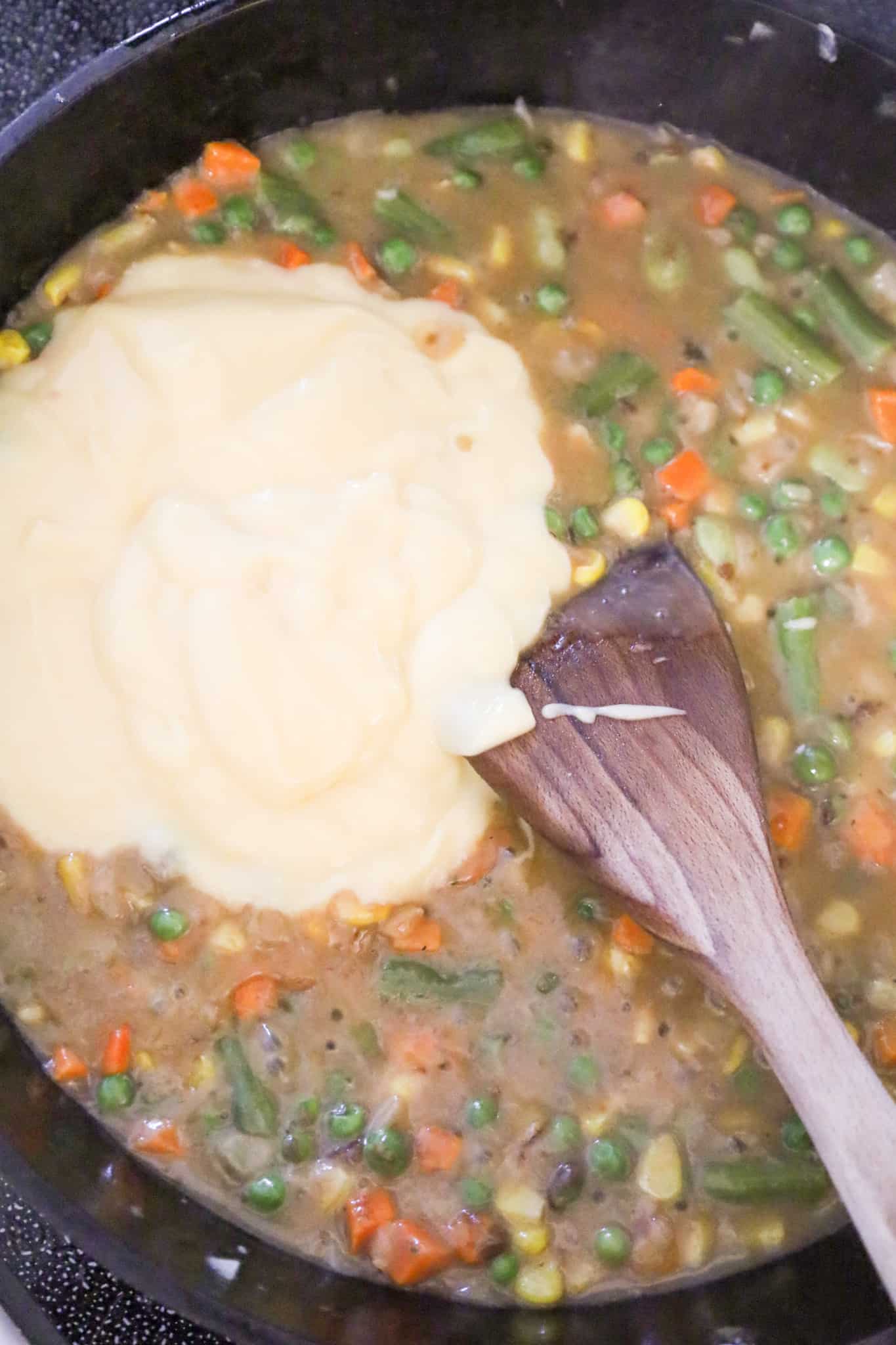 cream of chicken soup on top of vegetable and gravy mixture in a skillet