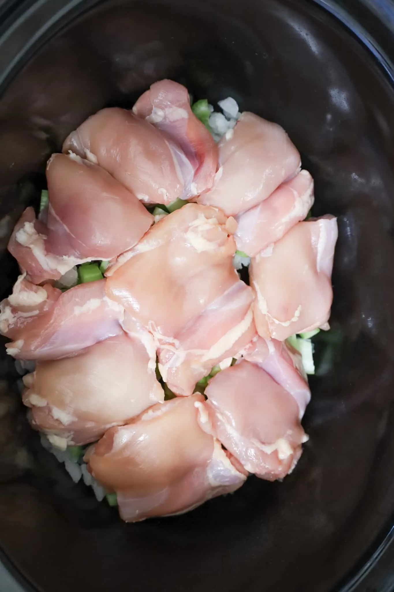 boneless, skinless chicken thighs on top of diced onions and celery in a crock pot