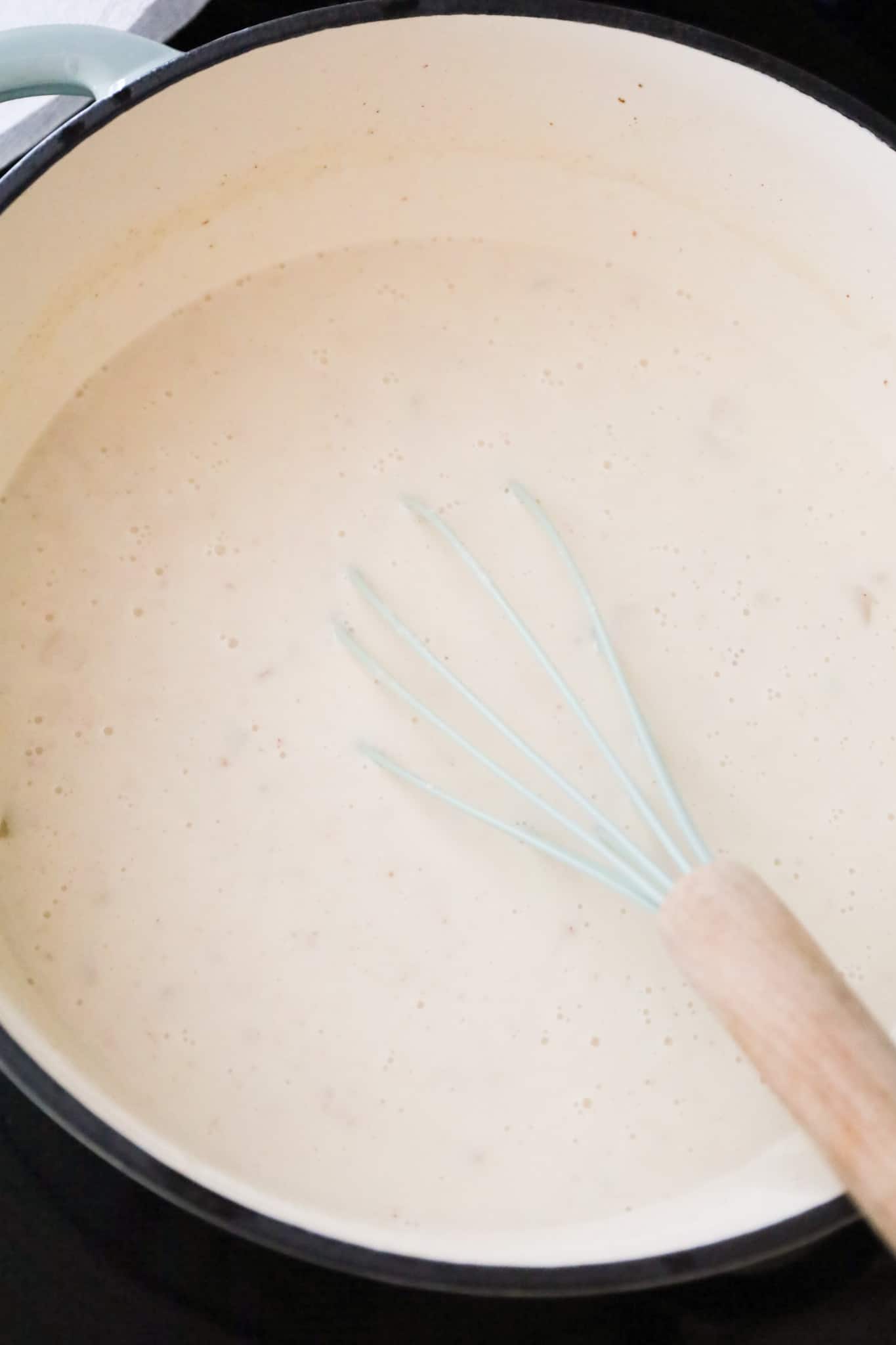whisking cream into broth mixture in a pot