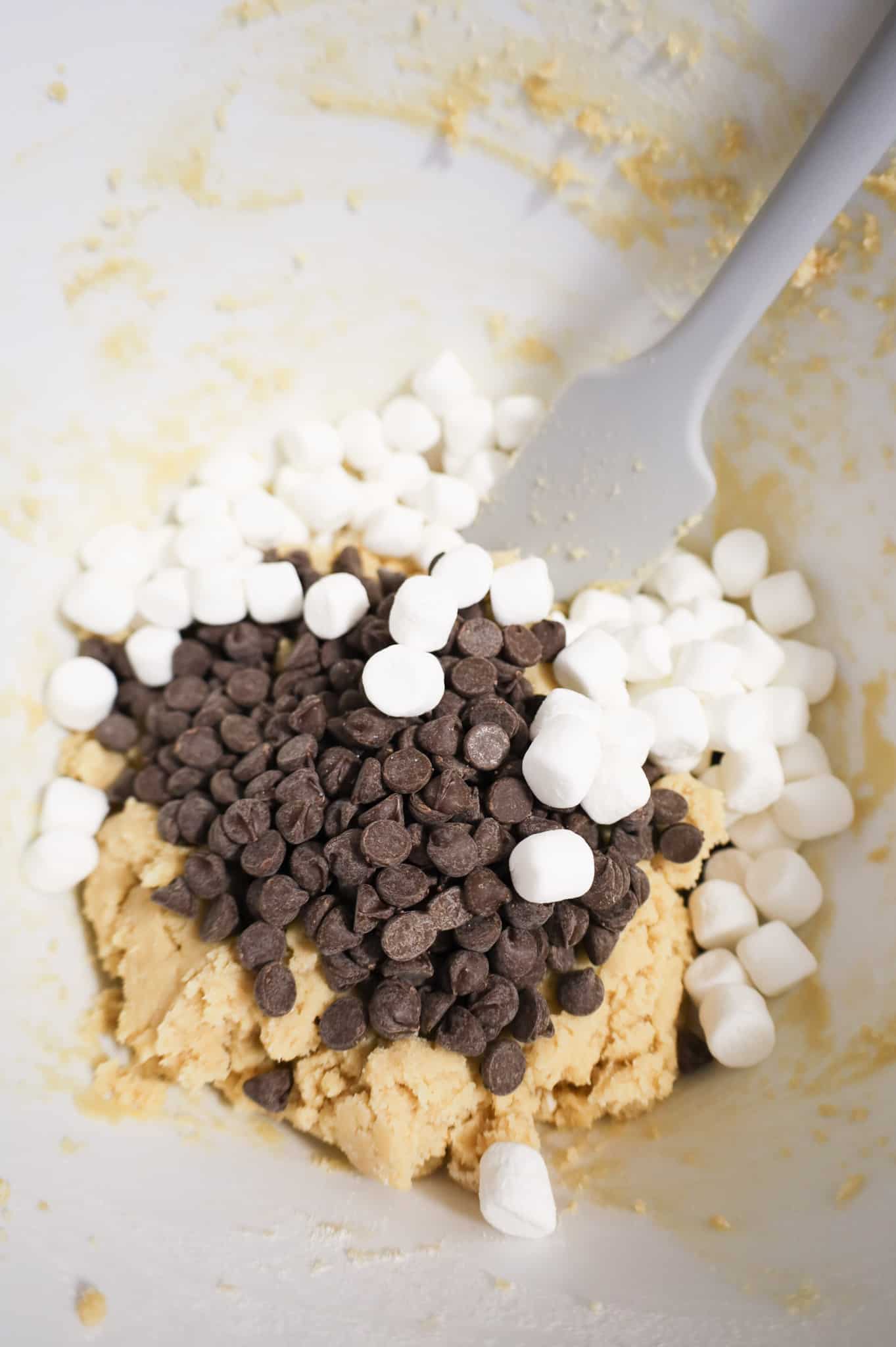 mini marshmallow and semi sweet chocolate chips on top of cookie dough in a mixing bowl