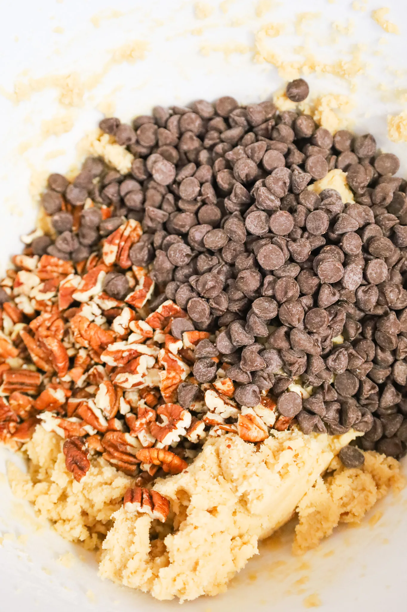 chopped pecans and semi sweet chocolate chips on top of cookie dough in a mixing bowl